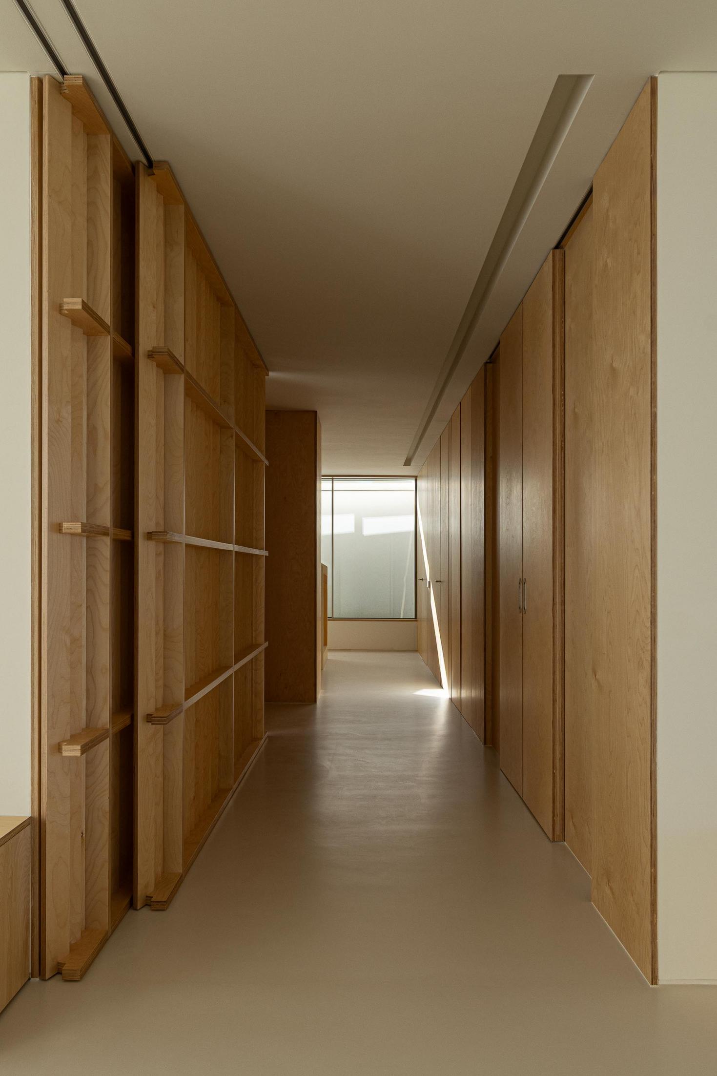 Corredor: Longo corredor com armários em madeira clara, pavimento claro e iluminação linear. — WEST CLIFFS D45 arquitetura ARX Portugal - Arquitectos em Óbidos