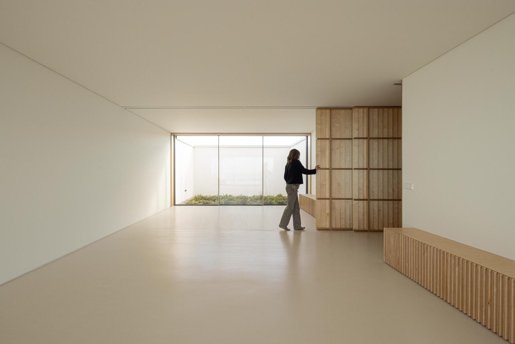 Sala: Espaçosa sala com divisória de madeira, pavimento claro e grande janela para o jardim interior. — WEST CLIFFS D45 arquitetura ARX Portugal - Arquitectos em Óbidos