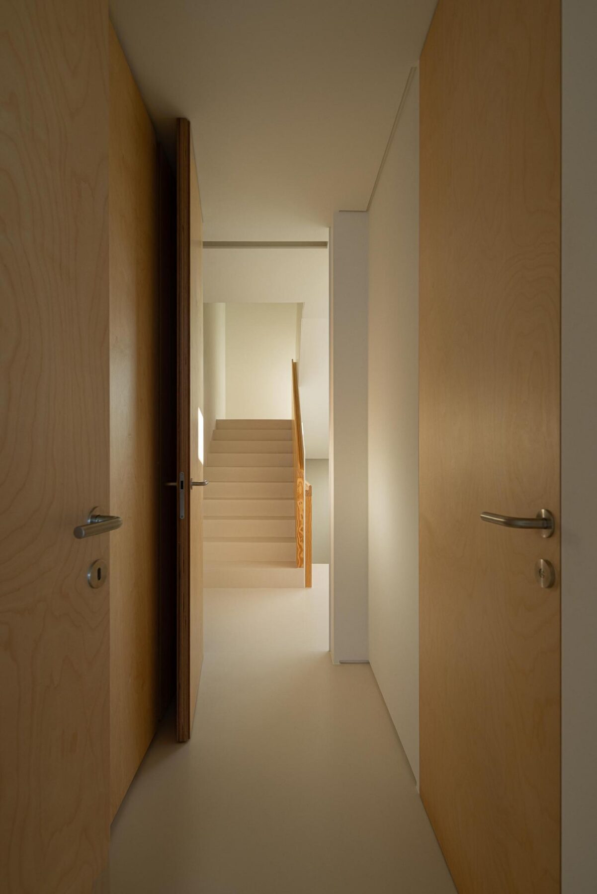 Corredor: Perspectiva do corredor com portas em madeira clara e acesso à escadaria. — WEST CLIFFS D45 arquitetura ARX Portugal - Arquitectos em Óbidos