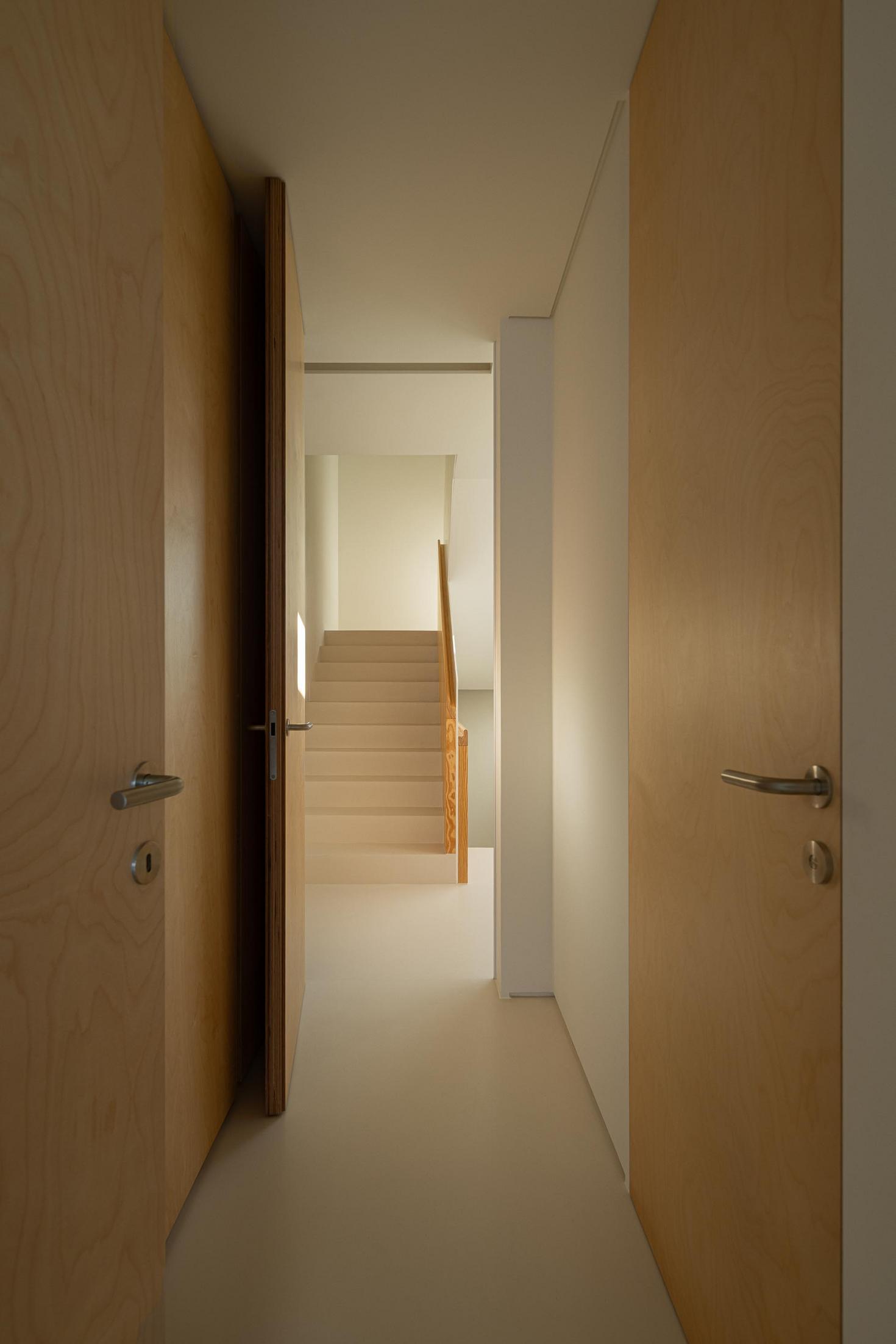 Corredor: Perspectiva do corredor com portas em madeira clara e acesso à escadaria. — WEST CLIFFS D45 arquitetura ARX Portugal - Arquitectos em Óbidos