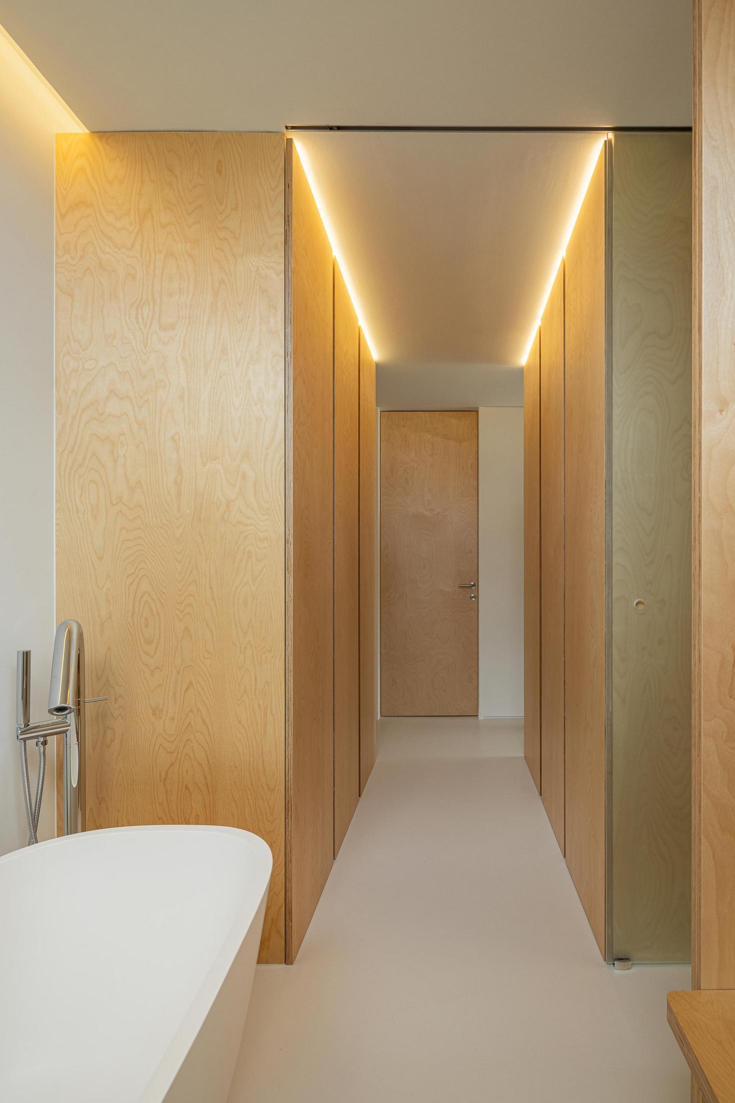 Casa de banho: Corredor de acesso à casa de banho com armários em madeira e iluminação linear. — WEST CLIFFS D45 arquitetura ARX Portugal - Arquitectos em Óbidos
