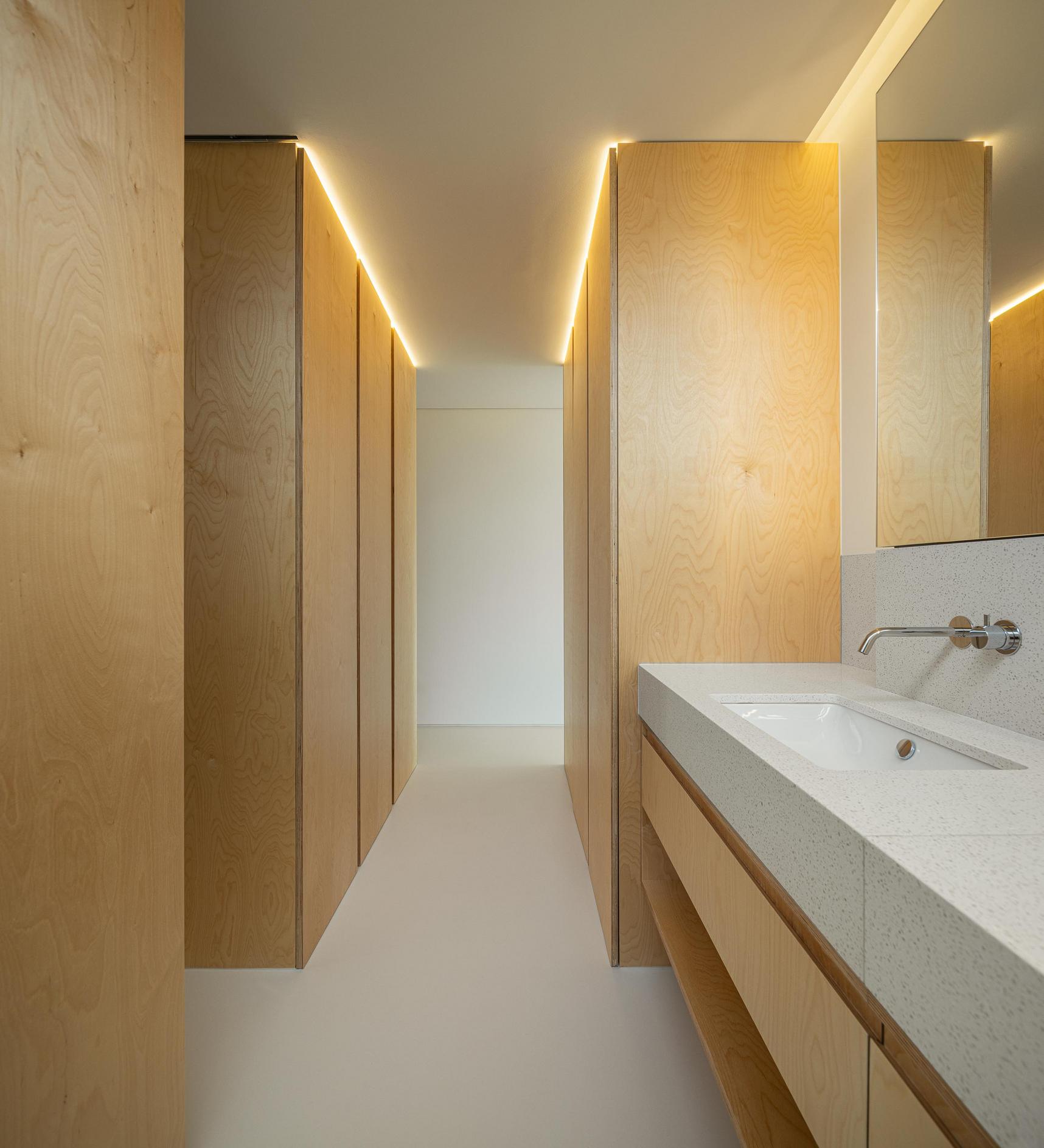 Casa de banho: Lavatório com bancada em pedra, armários em madeira e iluminação linear. — WEST CLIFFS D45 arquitetura ARX Portugal - Arquitectos em Óbidos