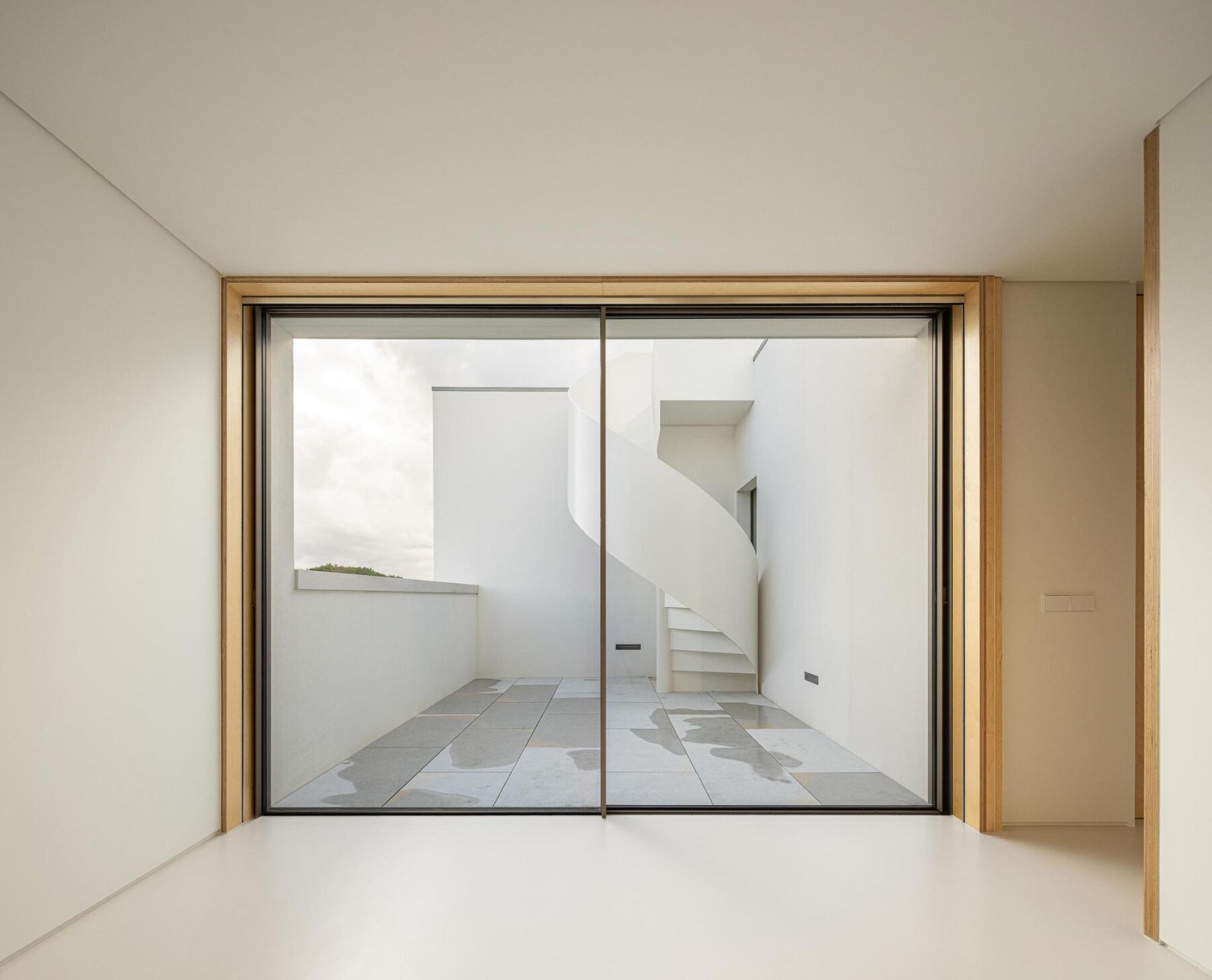 Hall: Janela panorâmica para pátio interior com escada em espiral e vegetação. — WEST CLIFFS D45 arquitetura ARX Portugal - Arquitectos em Óbidos