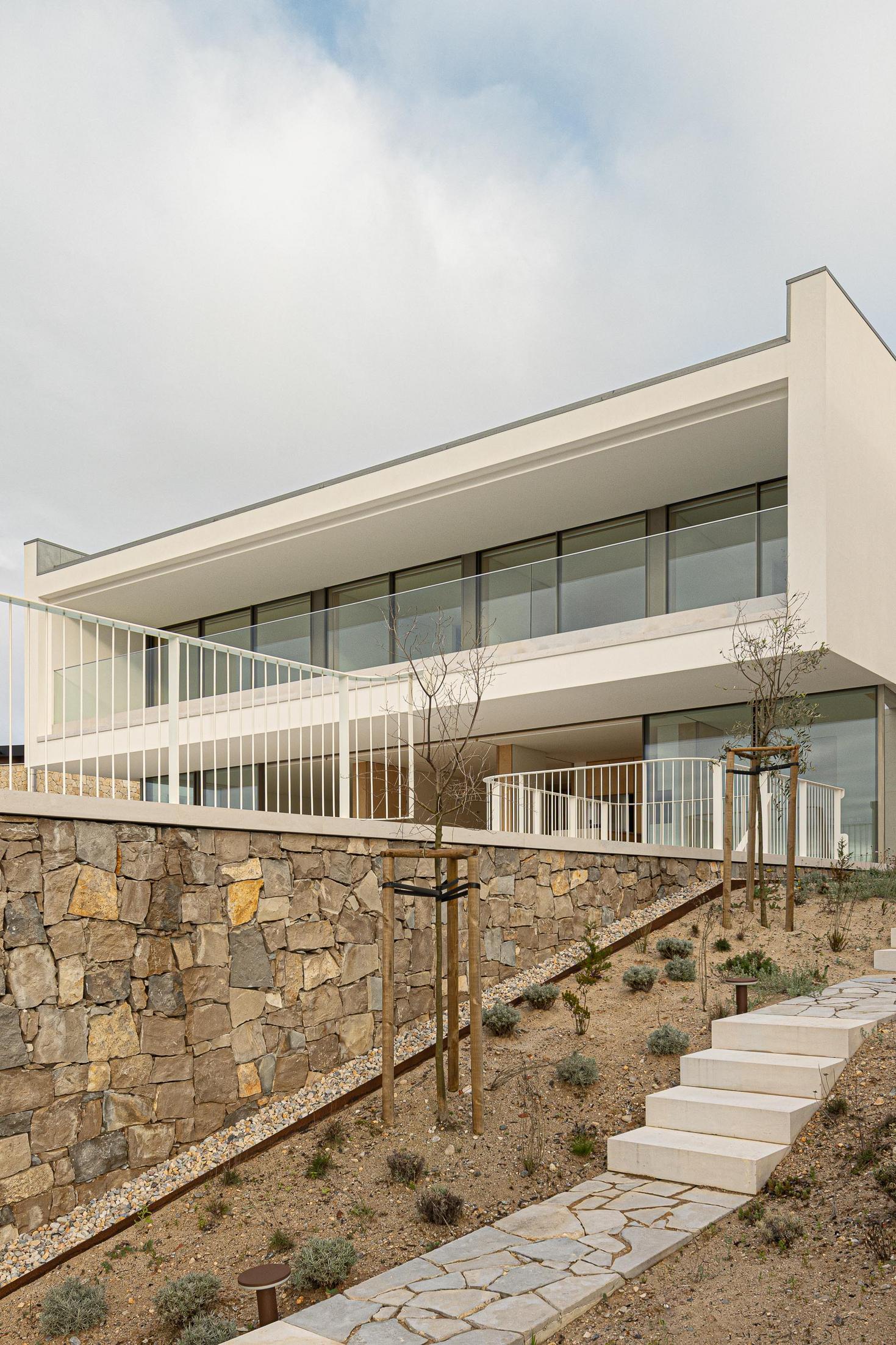 Jardim: Vista da casa com jardim, escadaria em pedra e fachada em pedra rústica. — WEST CLIFFS D45 arquitetura ARX Portugal - Arquitectos em Óbidos