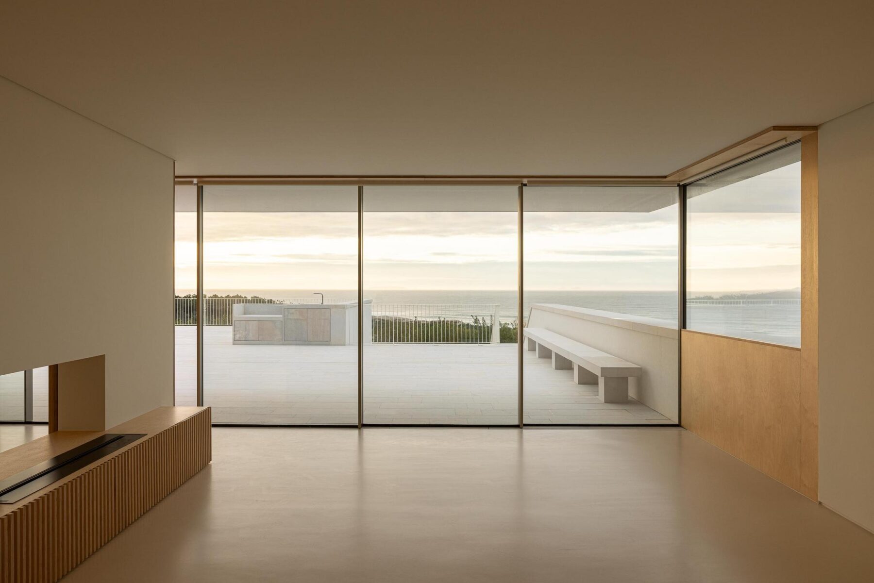 Sala: Sala de estar com grandes janelas, lareira embutida e vista para o terraço. — WEST CLIFFS D45 arquitetura ARX Portugal - Arquitectos em Óbidos