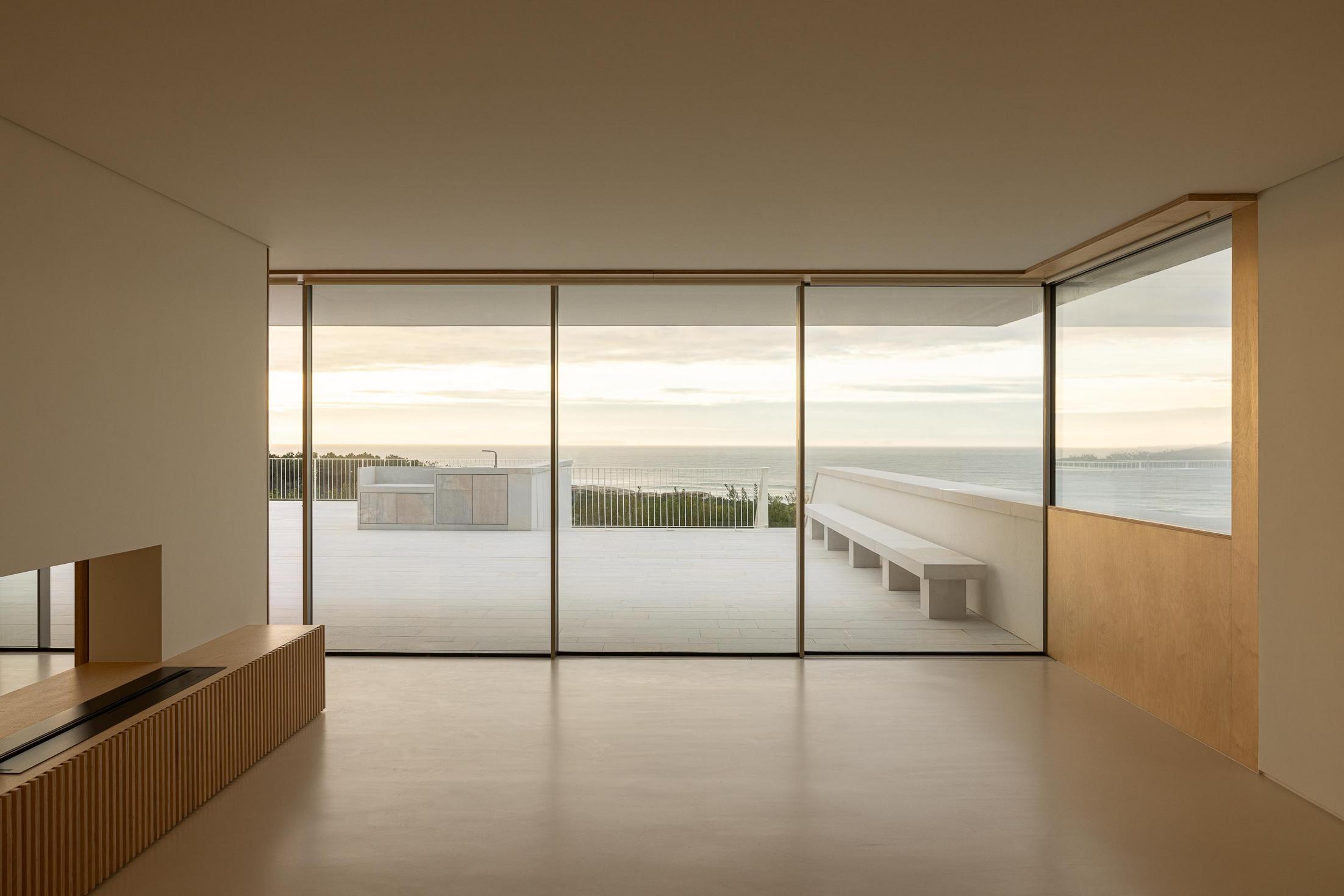 Sala: Sala de estar com grandes janelas, lareira embutida e vista para o terraço. — WEST CLIFFS D45 arquitetura ARX Portugal - Arquitectos em Óbidos