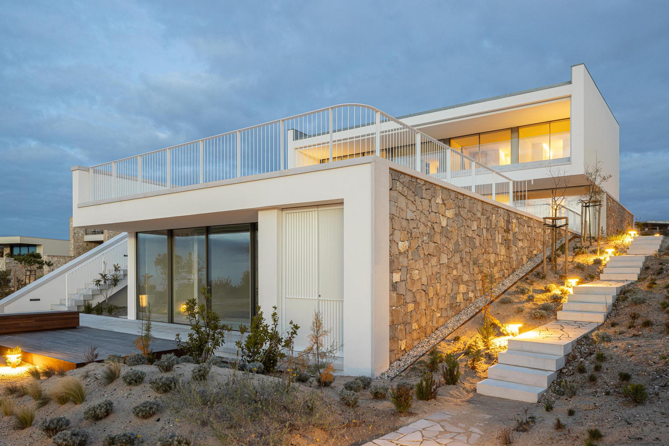 Fachada lateral: Vista noturna da casa com jardim, escadaria e iluminação exterior. — WEST CLIFFS D45 arquitetura ARX Portugal - Arquitectos em Óbidos