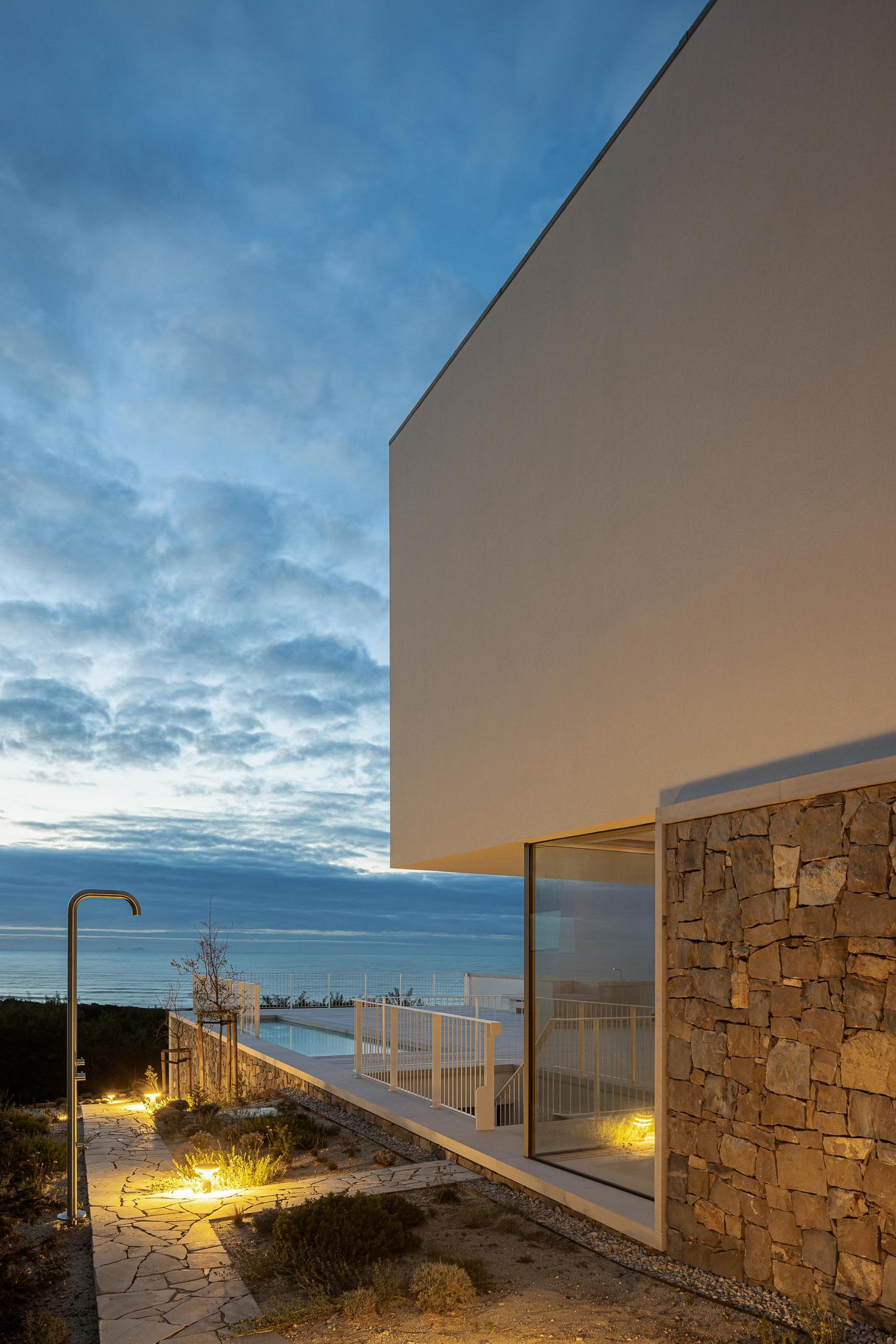 Jardim: Vista noturna da casa com jardim, caminho em pedra e iluminação exterior. — WEST CLIFFS D45 arquitetura ARX Portugal - Arquitectos em Óbidos