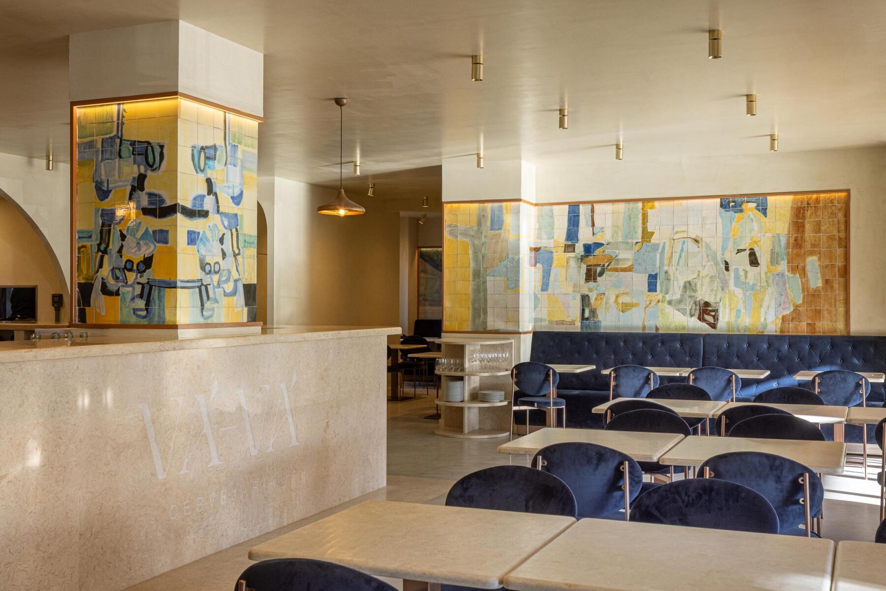 Salão: Vista geral com balcão em pedra, painel de azulejos coloridos, mesas de mármore e cadeiras de veludo azul. — Cervejaria Vává - Requalificação arquitetura Rethorica Studio em Lisboa