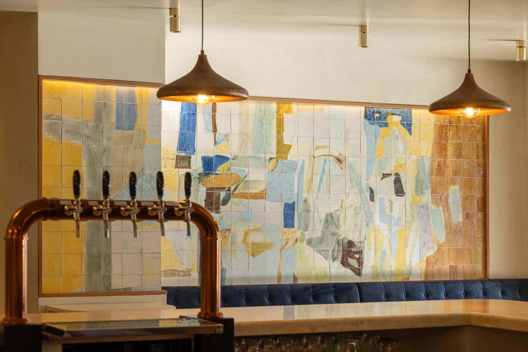 Salão: Balcão com torneiras de cerveja em cobre, painel de azulejos e candeeiros suspensos em metal. — Cervejaria Vává - Requalificação arquitetura Rethorica Studio em Lisboa