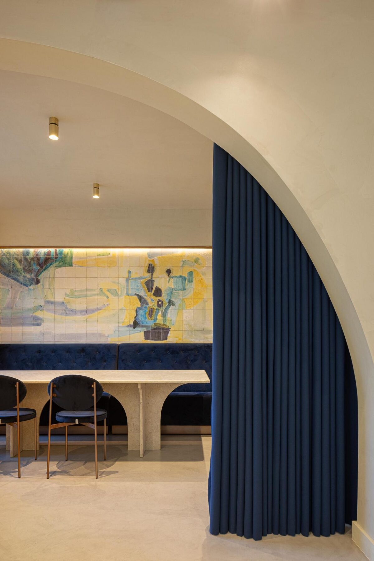 Salão: Detalhe de mesa com base em pedra, cadeiras de veludo azul e cortina azul escura. — Cervejaria Vává - Requalificação arquitetura Rethorica Studio em Lisboa