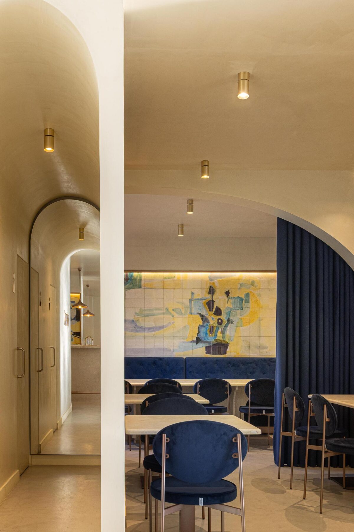 Corredor: Arcos em sequência, pavimento em cimento afagado, cadeiras de veludo azul e candeeiros embutidos. — Cervejaria Vává - Requalificação arquitetura Rethorica Studio em Lisboa