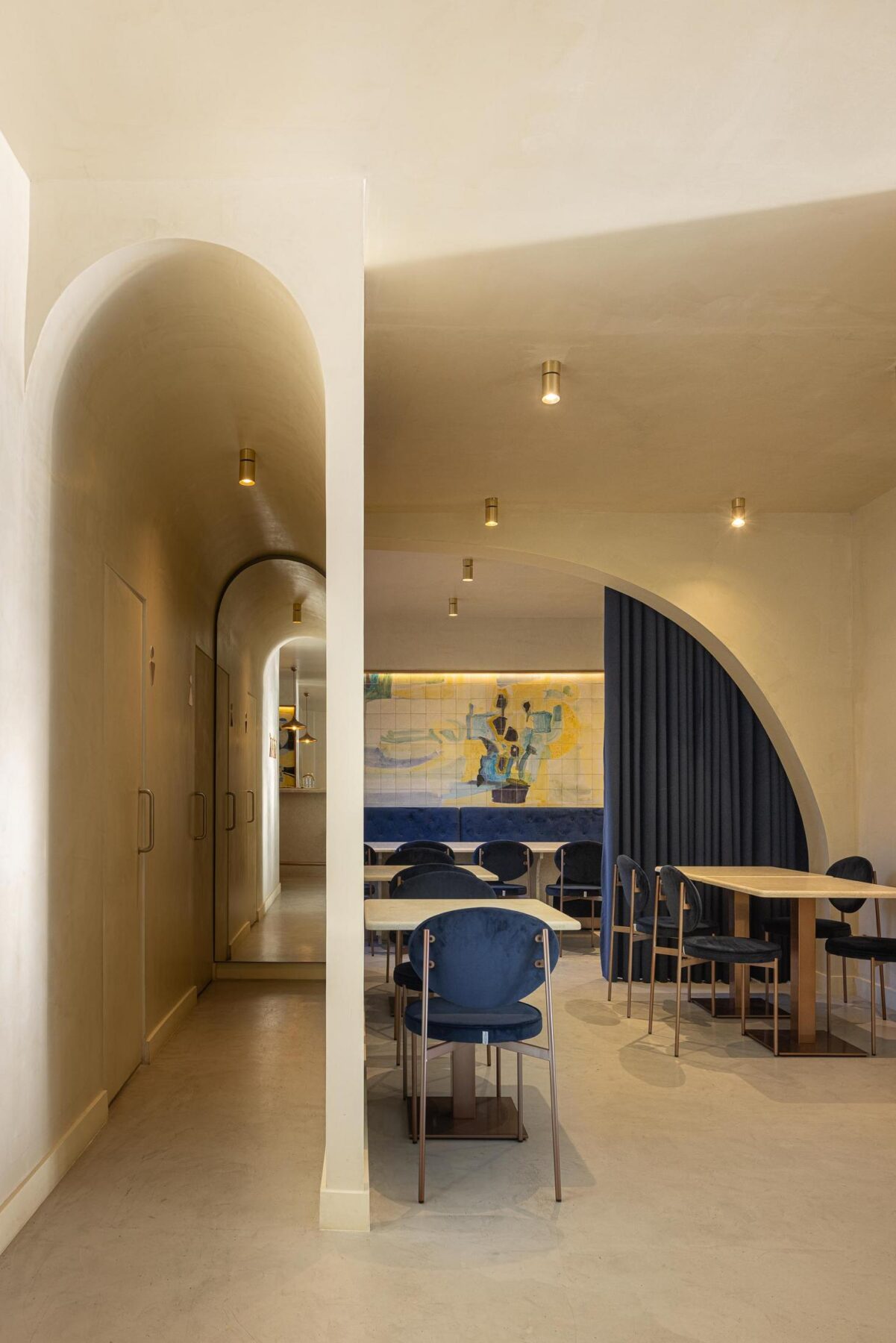 Corredor: Arcos em sequência, pavimento em cimento afagado, cadeiras de veludo azul e candeeiros embutidos. — Cervejaria Vává - Requalificação arquitetura Rethorica Studio em Lisboa