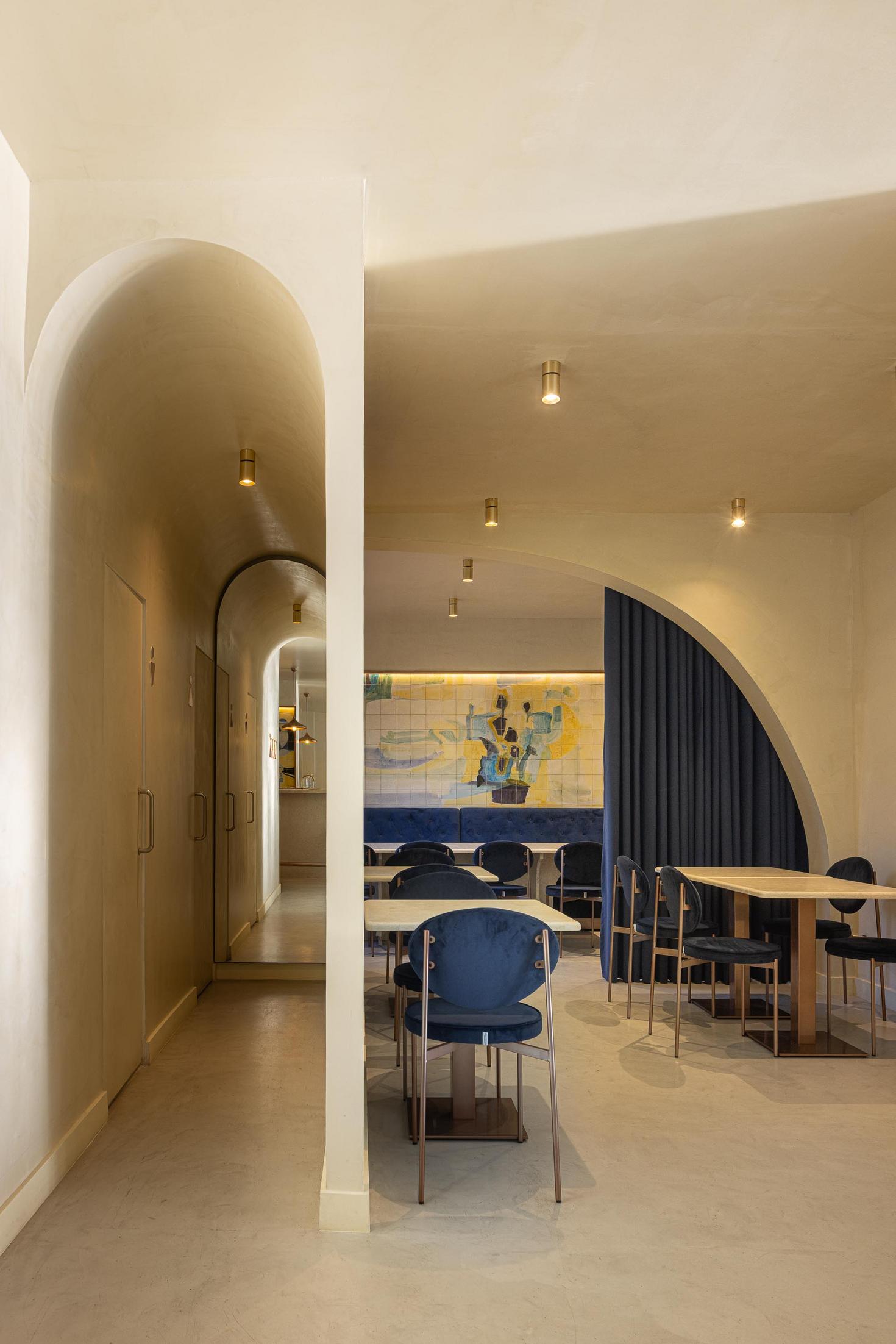 Corredor: Arcos em sequência, pavimento em cimento afagado, cadeiras de veludo azul e candeeiros embutidos. — Cervejaria Vává - Requalificação arquitetura Rethorica Studio em Lisboa