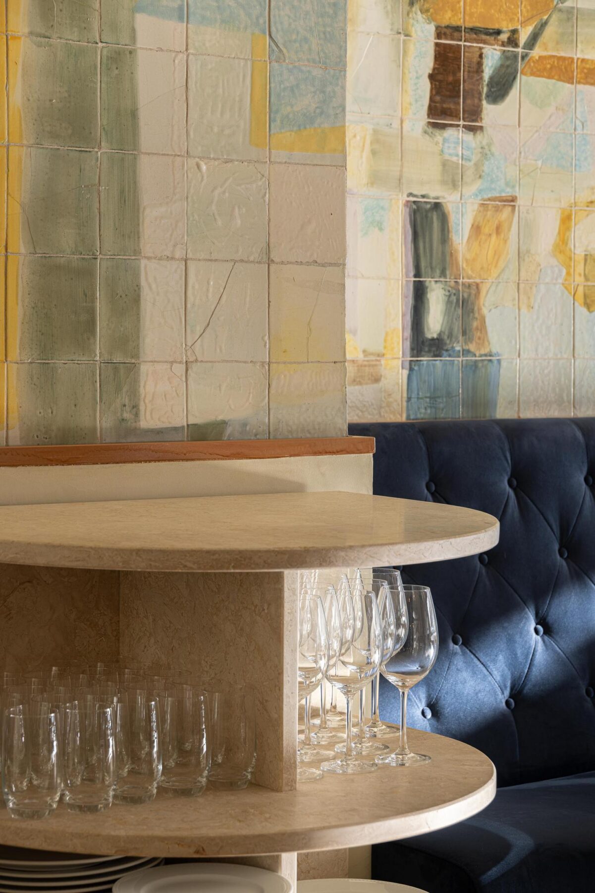 Salão: Detalhe da prateleira com louça e copos, sofá corrido de veludo azul e painel de azulejos. — Cervejaria Vává - Requalificação arquitetura Rethorica Studio em Lisboa