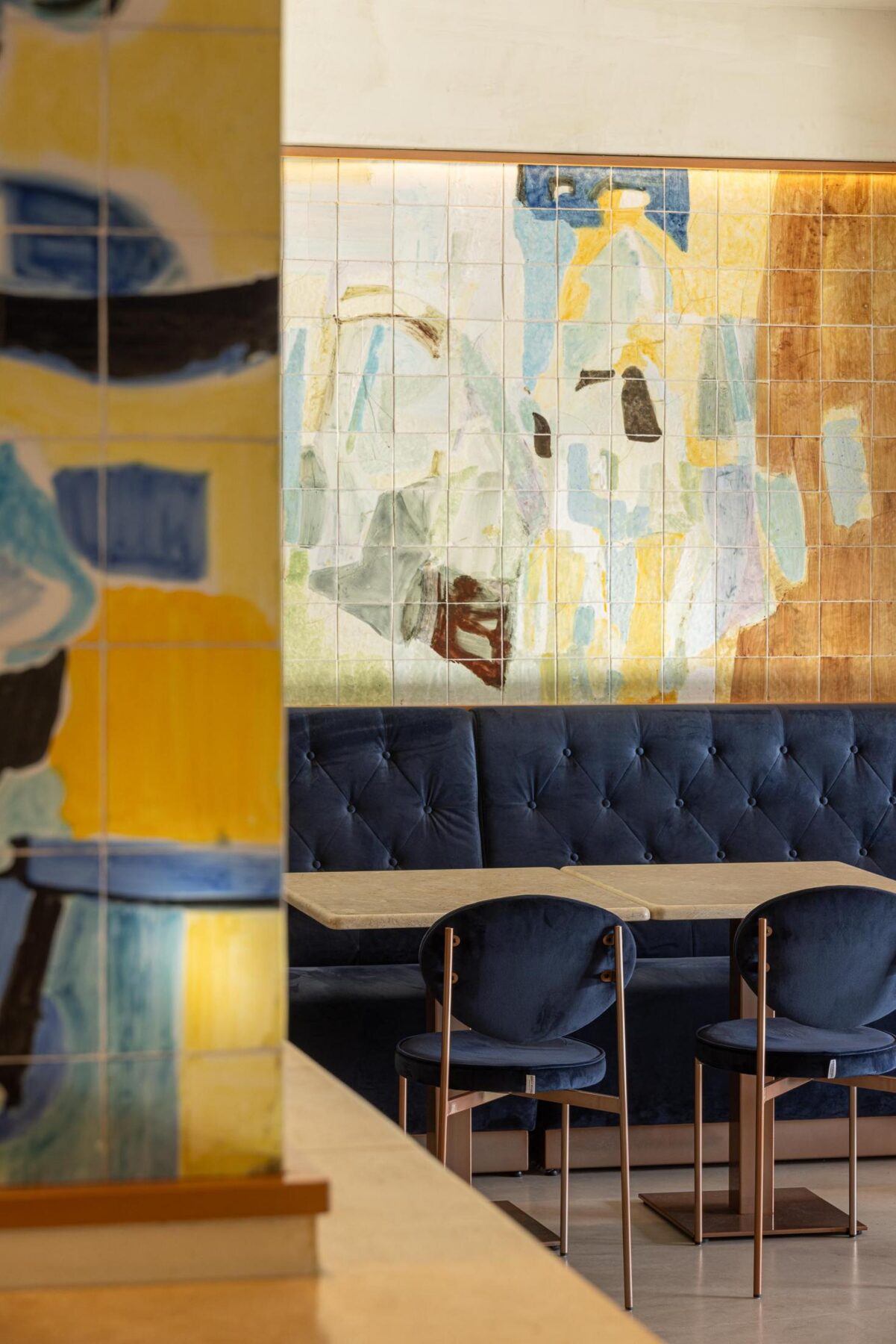 Salão: Detalhe do painel de azulejos, sofá corrido de veludo azul e mesas com cadeiras. — Cervejaria Vává - Requalificação arquitetura Rethorica Studio em Lisboa