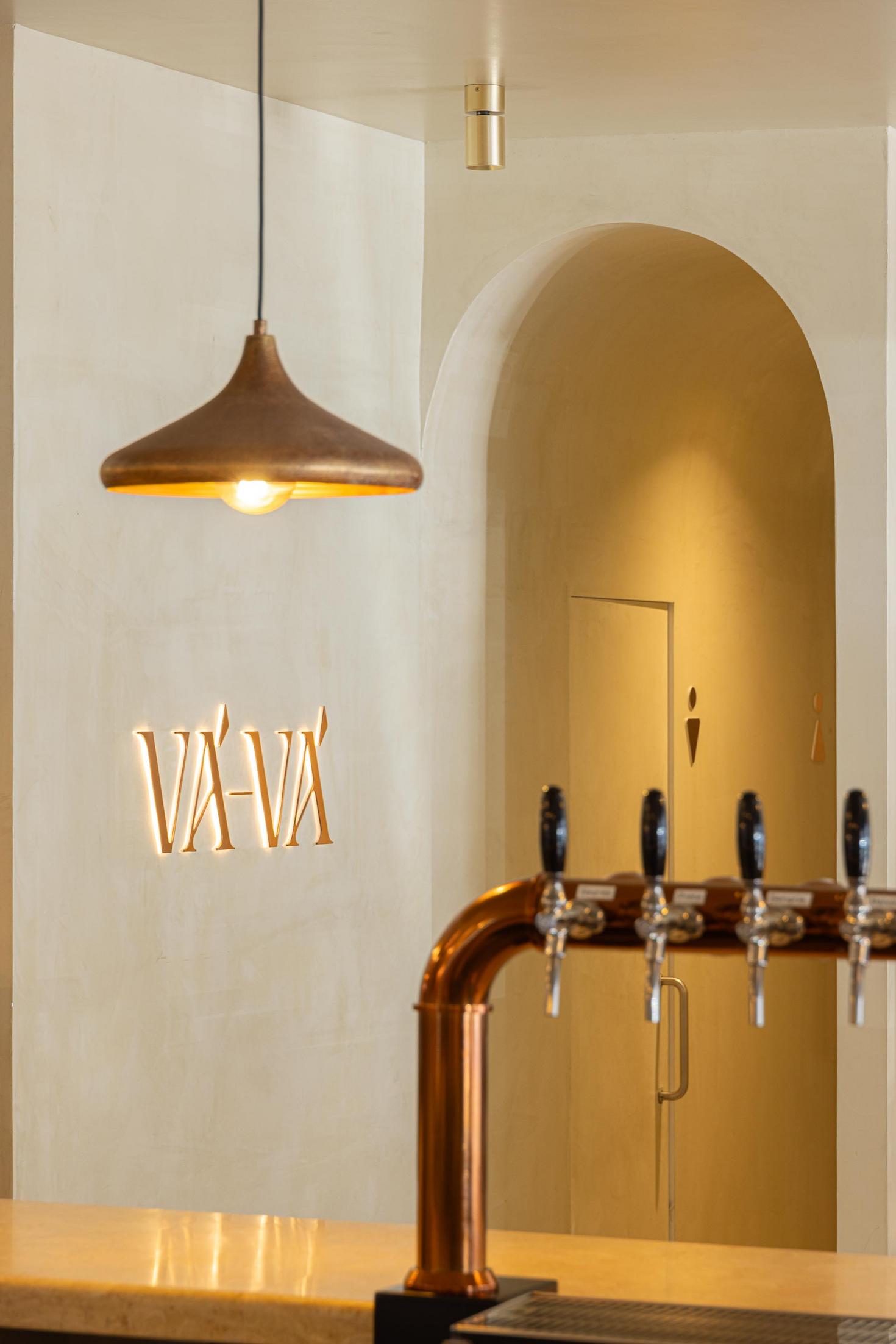 Balcão: Torneiras de cerveja em cobre, candeeiro suspenso e sinalética "Vá-Vá" na parede. — Cervejaria Vává - Requalificação arquitetura Rethorica Studio em Lisboa