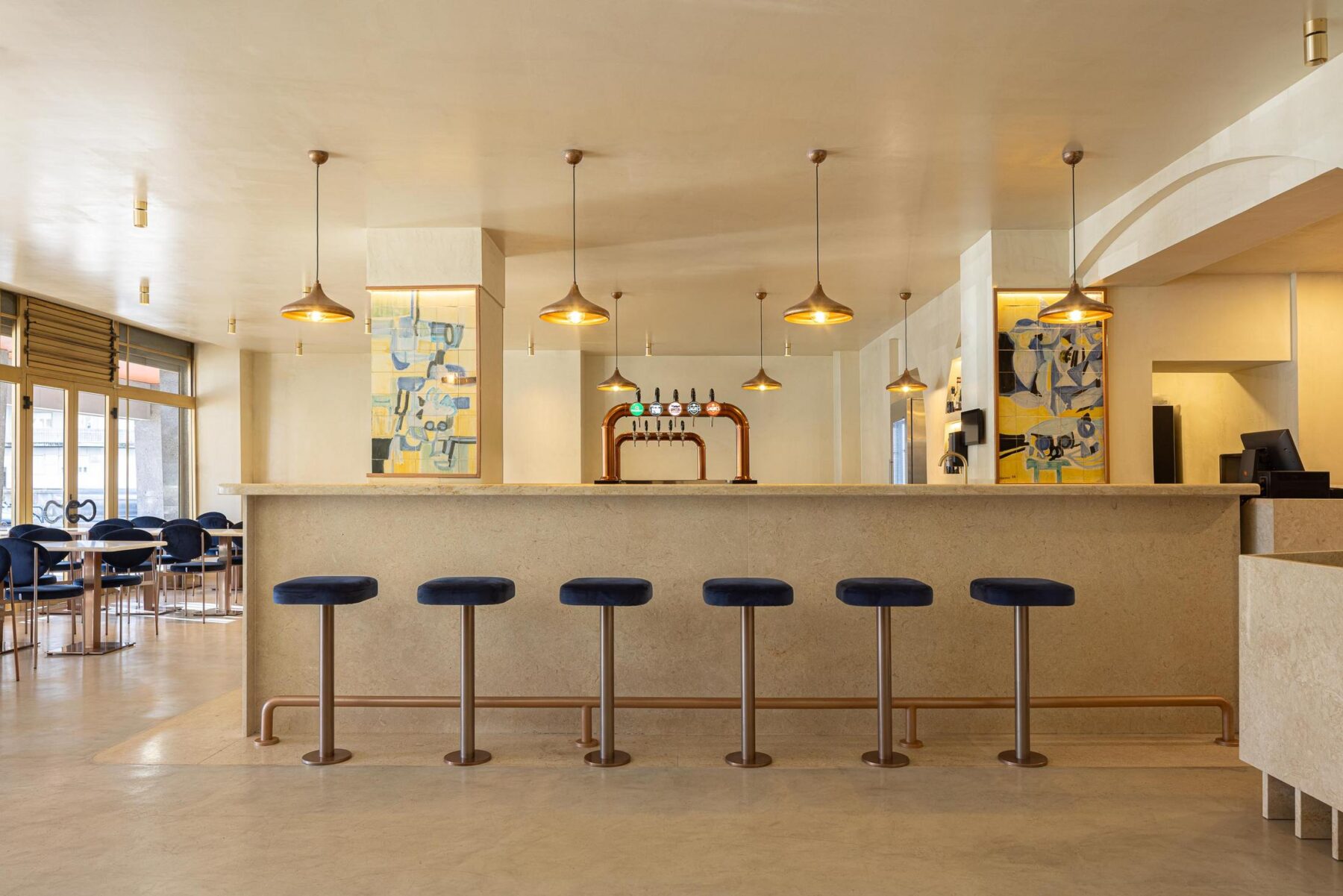 Salão: Vista geral do balcão com bancos altos, painéis de azulejos e mesas com cadeiras. — Cervejaria Vává - Requalificação arquitetura Rethorica Studio em Lisboa
