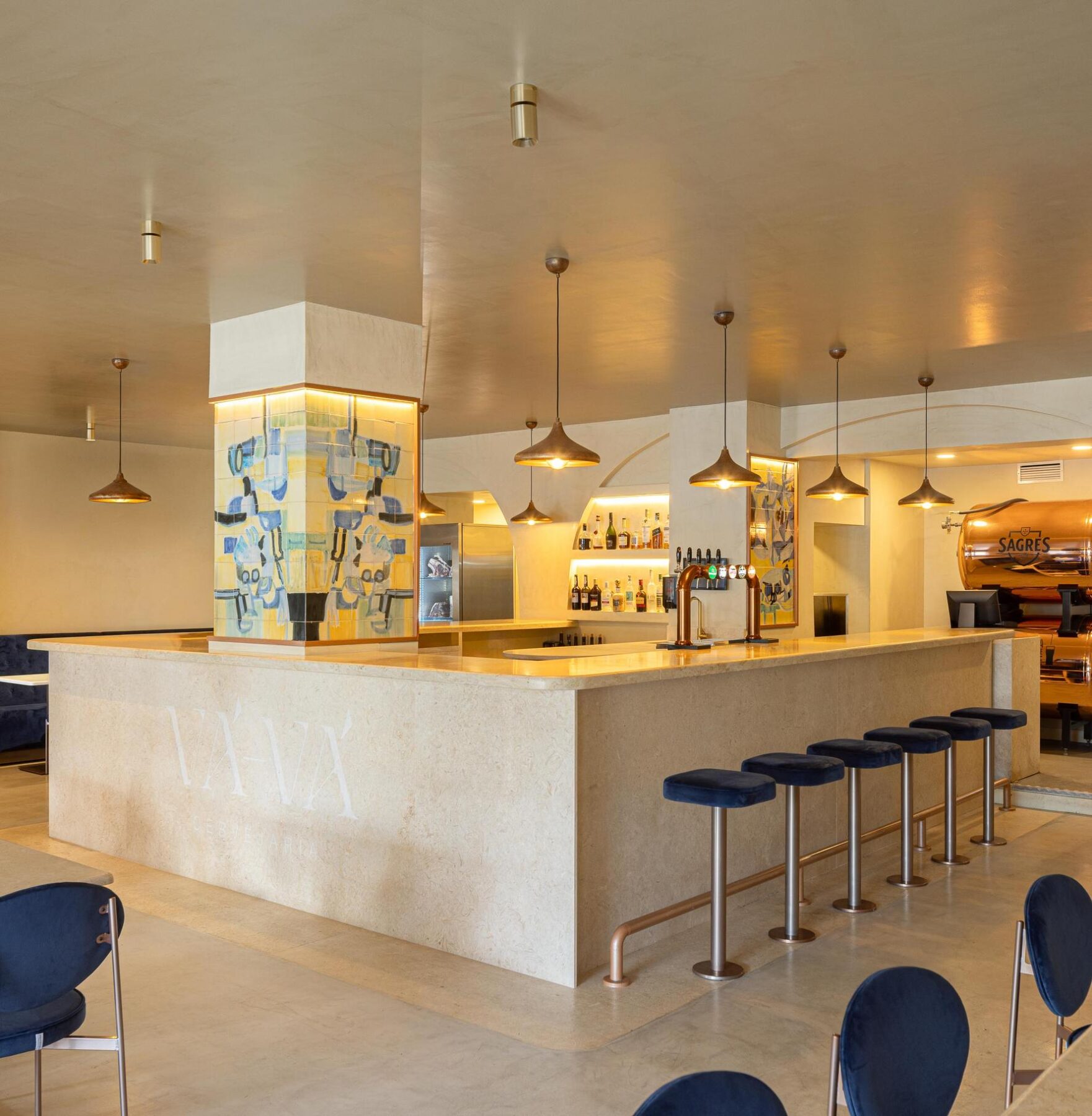 Balcão: Balcão em pedra clara com bancos altos de veludo azul, painel de azulejos e garrafeira. — Cervejaria Vává - Requalificação arquitetura Rethorica Studio em Lisboa