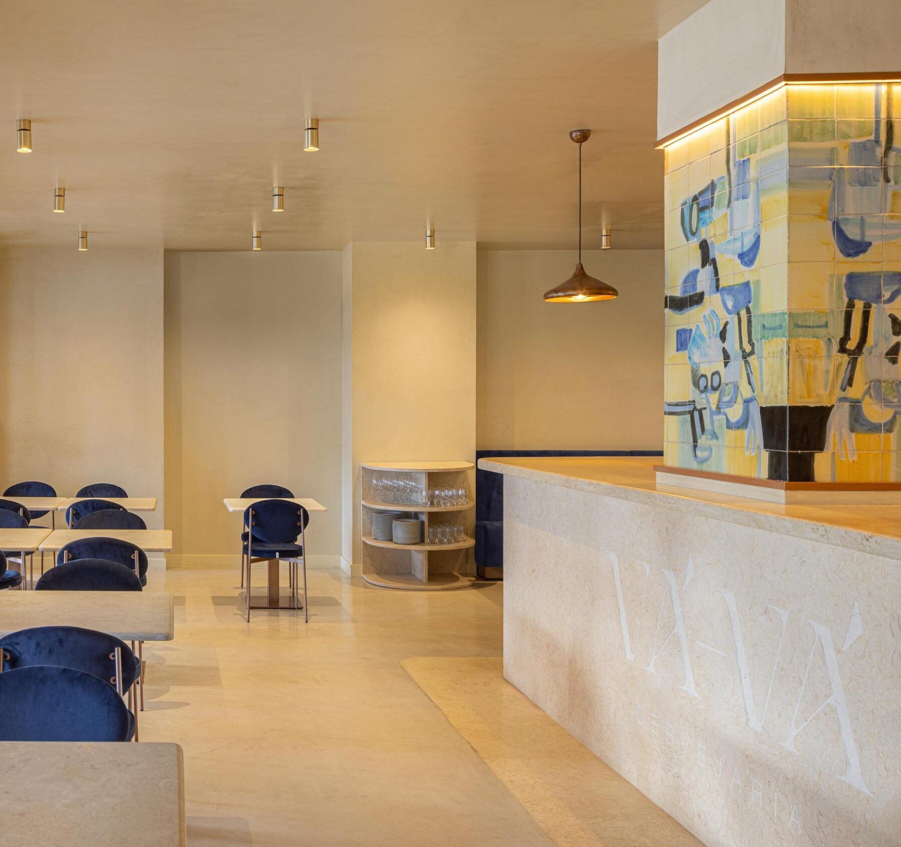 Salão: Balcão em pedra clara, cadeiras de veludo azul e painel de azulejos. — Cervejaria Vává - Requalificação arquitetura Rethorica Studio em Lisboa