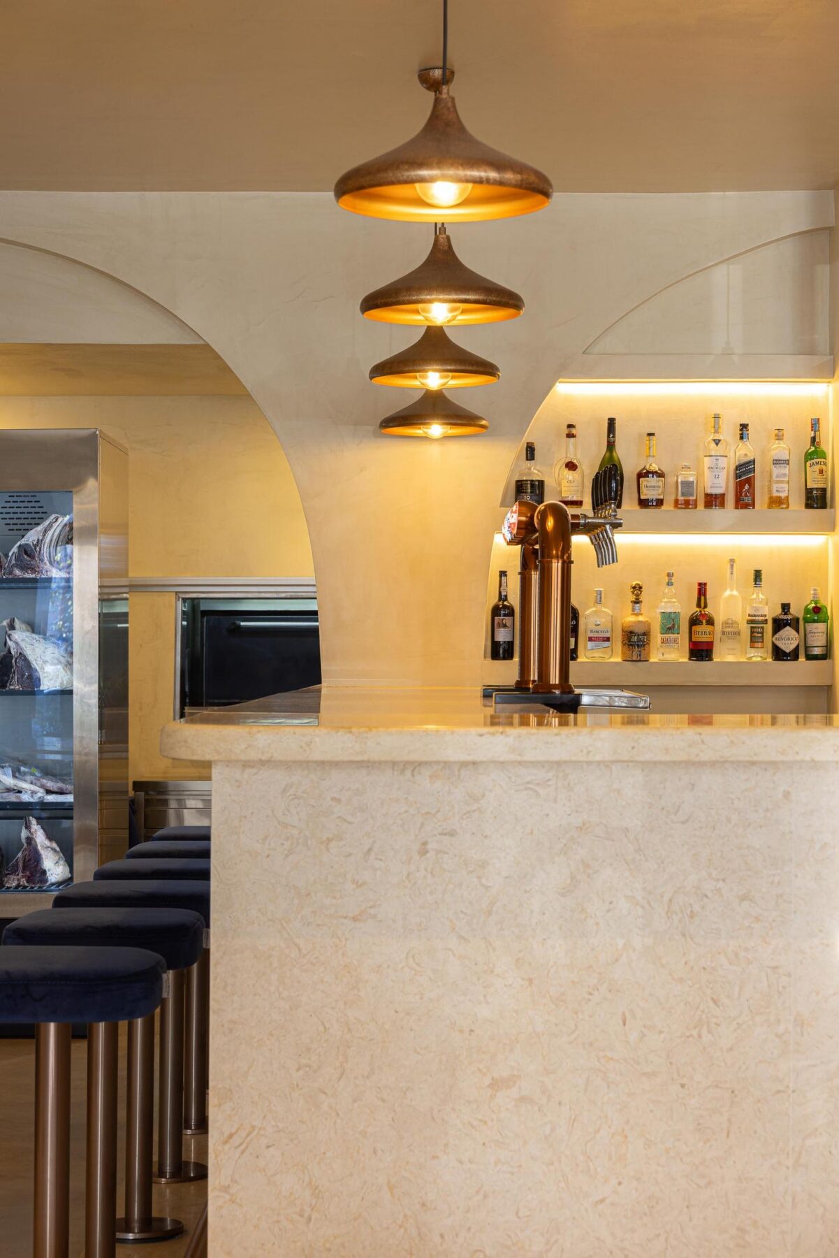 Balcão: Detalhe do balcão com garrafeira iluminada e bancos altos de veludo azul. — Cervejaria Vává - Requalificação arquitetura Rethorica Studio em Lisboa