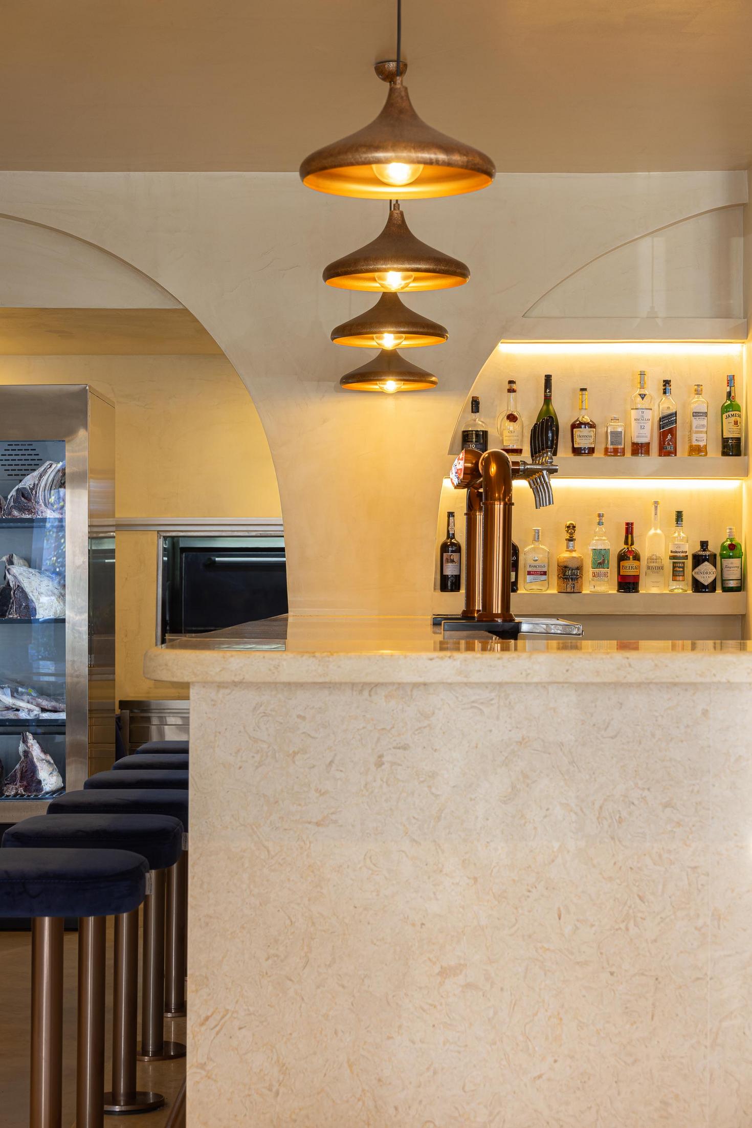 Balcão: Detalhe do balcão com garrafeira iluminada e bancos altos de veludo azul. — Cervejaria Vává - Requalificação arquitetura Rethorica Studio em Lisboa