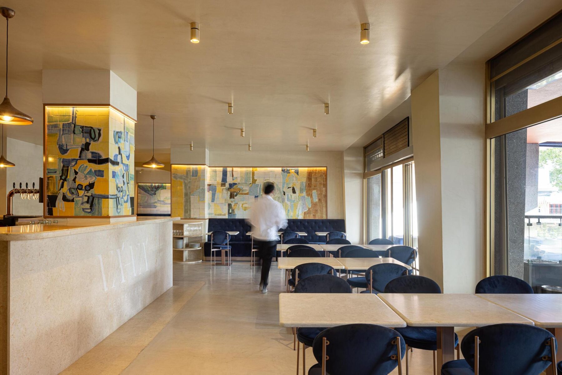 Salão: Vista geral do salão com balcão, painel de azulejos, mesas e cadeiras de veludo azul. — Cervejaria Vává - Requalificação arquitetura Rethorica Studio em Lisboa