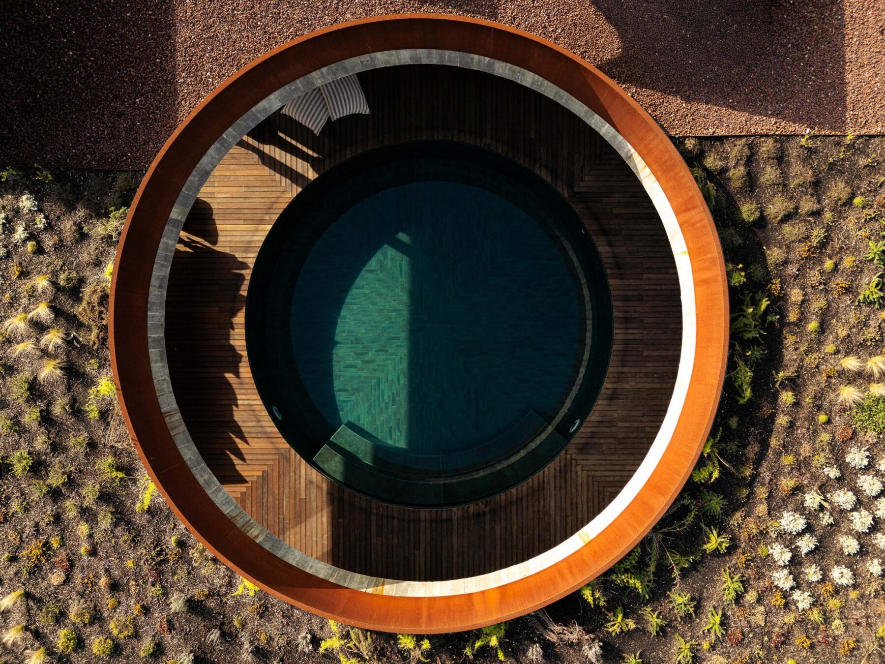 Vista superior da piscina circular, rodeada por deck de madeira e jardim com seixo e vegetação. — Mimosa House arquitetura Pedro Henrique Arquitecto em Esmoriz