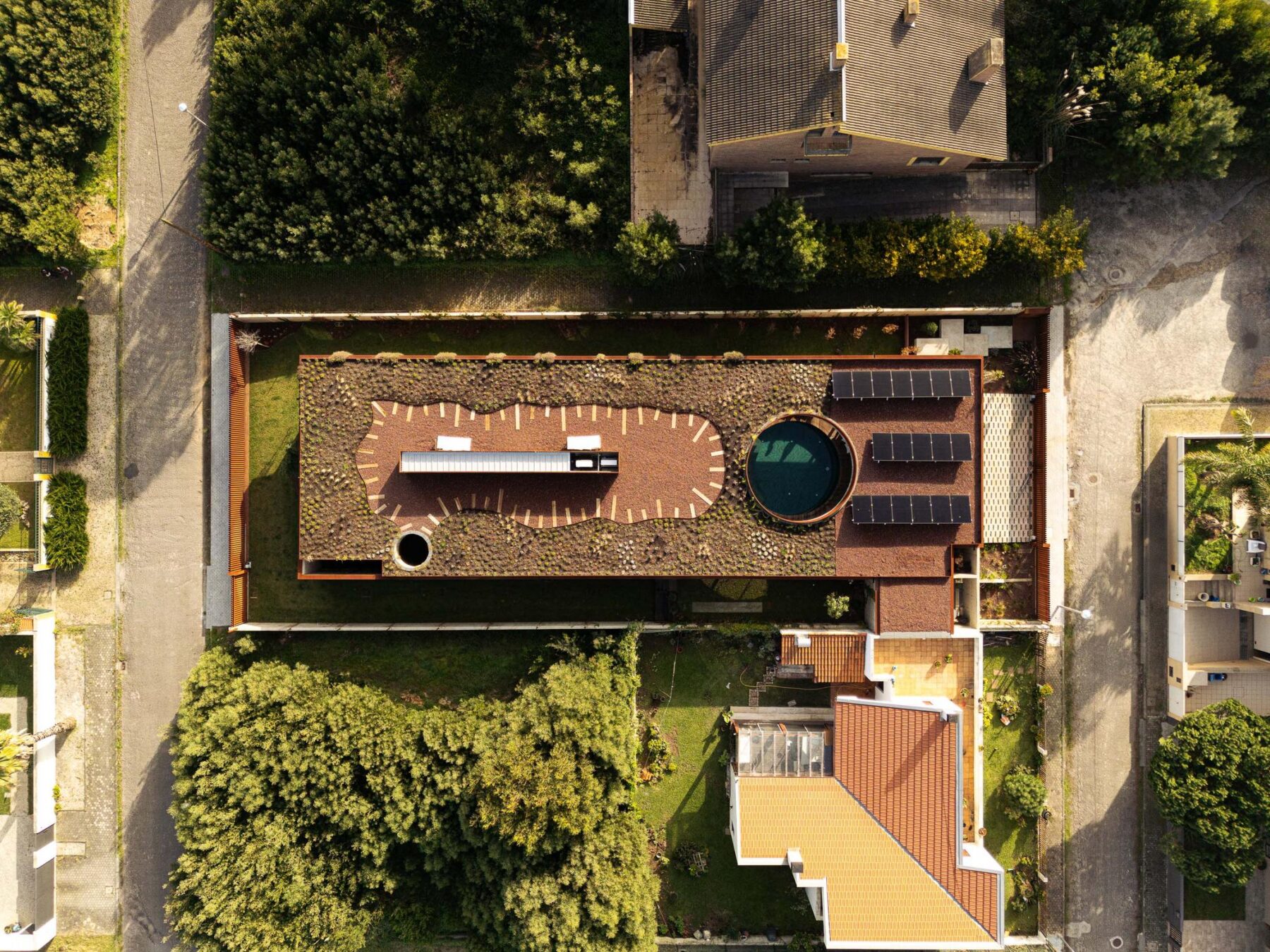 Vista aérea da casa com telhado ajardinado, piscina circular, painéis solares e envolvente urbana. — Mimosa House arquitetura Pedro Henrique Arquitecto em Esmoriz