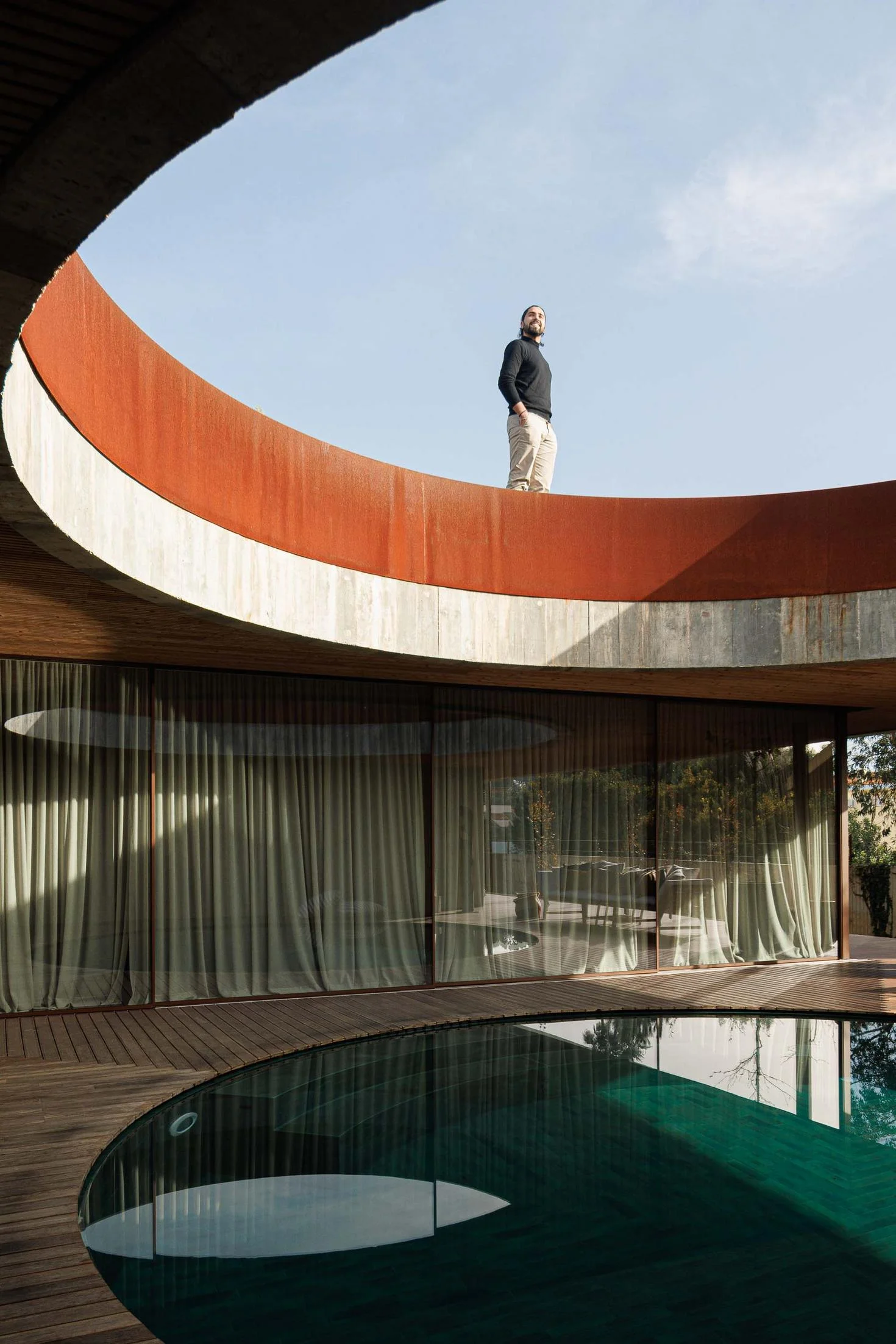 Piscina circular com borda em aço corten, deck de madeira e cortinas translúcidas nas janelas. — Mimosa House arquitetura Pedro Henrique Arquitecto em Esmoriz
