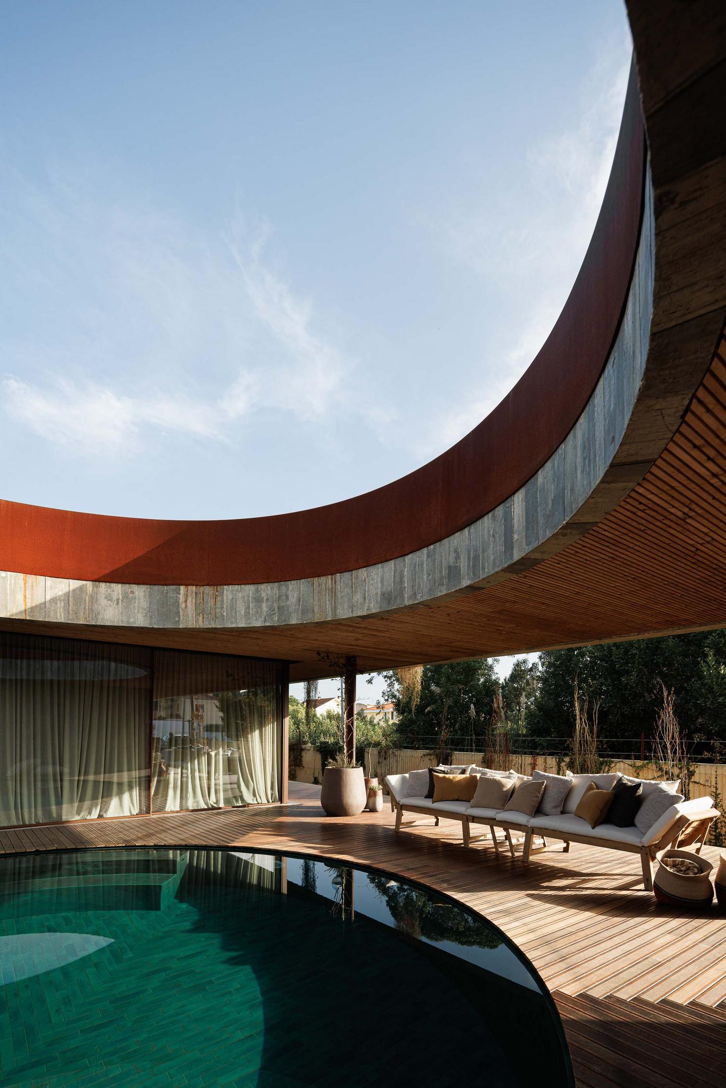Área de estar exterior junto à piscina, com sofás confortáveis e teto em madeira ripada. — Mimosa House arquitetura Pedro Henrique Arquitecto em Esmoriz