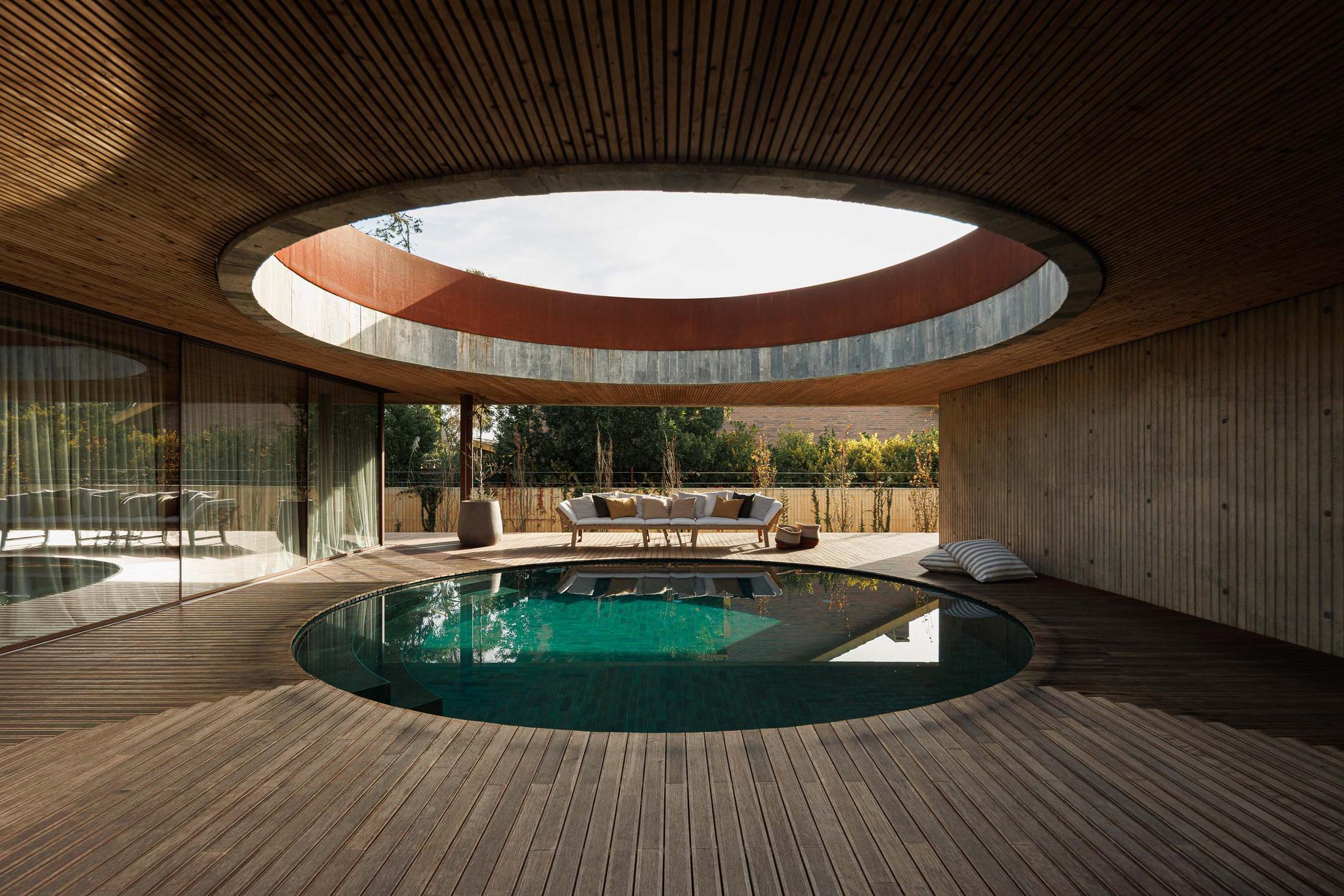 Vista geral da piscina circular, com deck de madeira, teto ripado e mobiliário de exterior. — Mimosa House arquitetura Pedro Henrique Arquitecto em Esmoriz