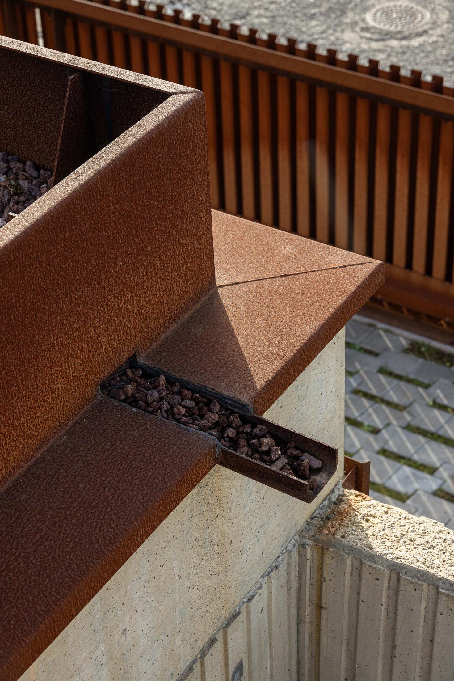 Detalhe de um vaso em aço corten com pedras decorativas, junto a uma vedação ripada. — Mimosa House arquitetura Pedro Henrique Arquitecto em Esmoriz