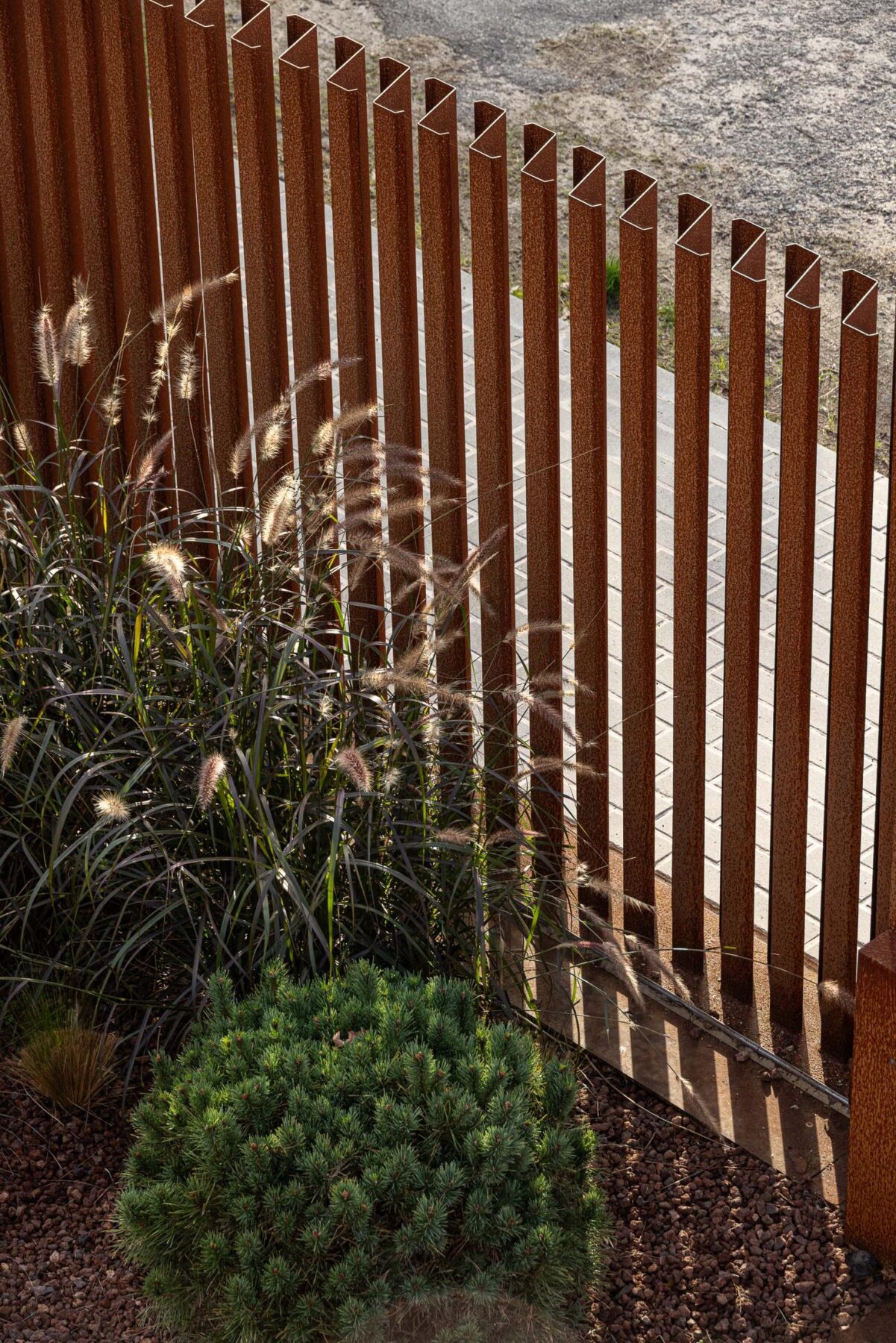 Vedação em ripas de aço corten, com vegetação ornamental e pavimento em grelha. — Mimosa House arquitetura Pedro Henrique Arquitecto em Esmoriz