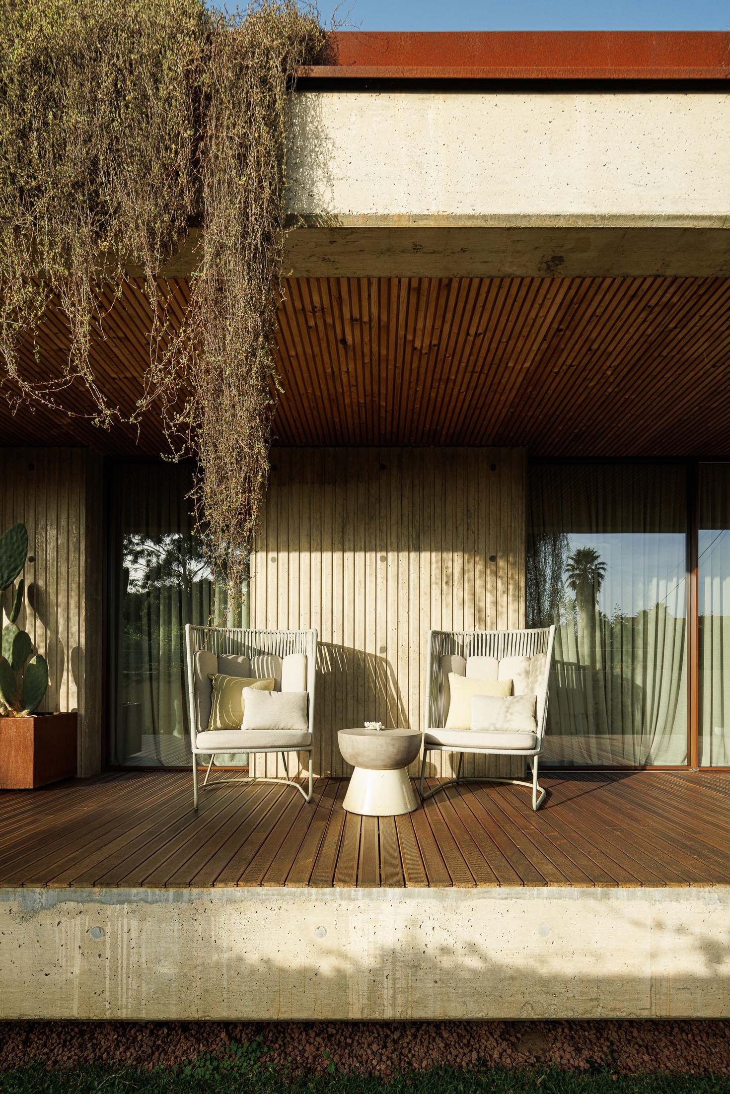 Detalhe da varanda com cadeiras de exterior, mesa de apoio e teto em madeira ripada. — Mimosa House arquitetura Pedro Henrique Arquitecto em Esmoriz