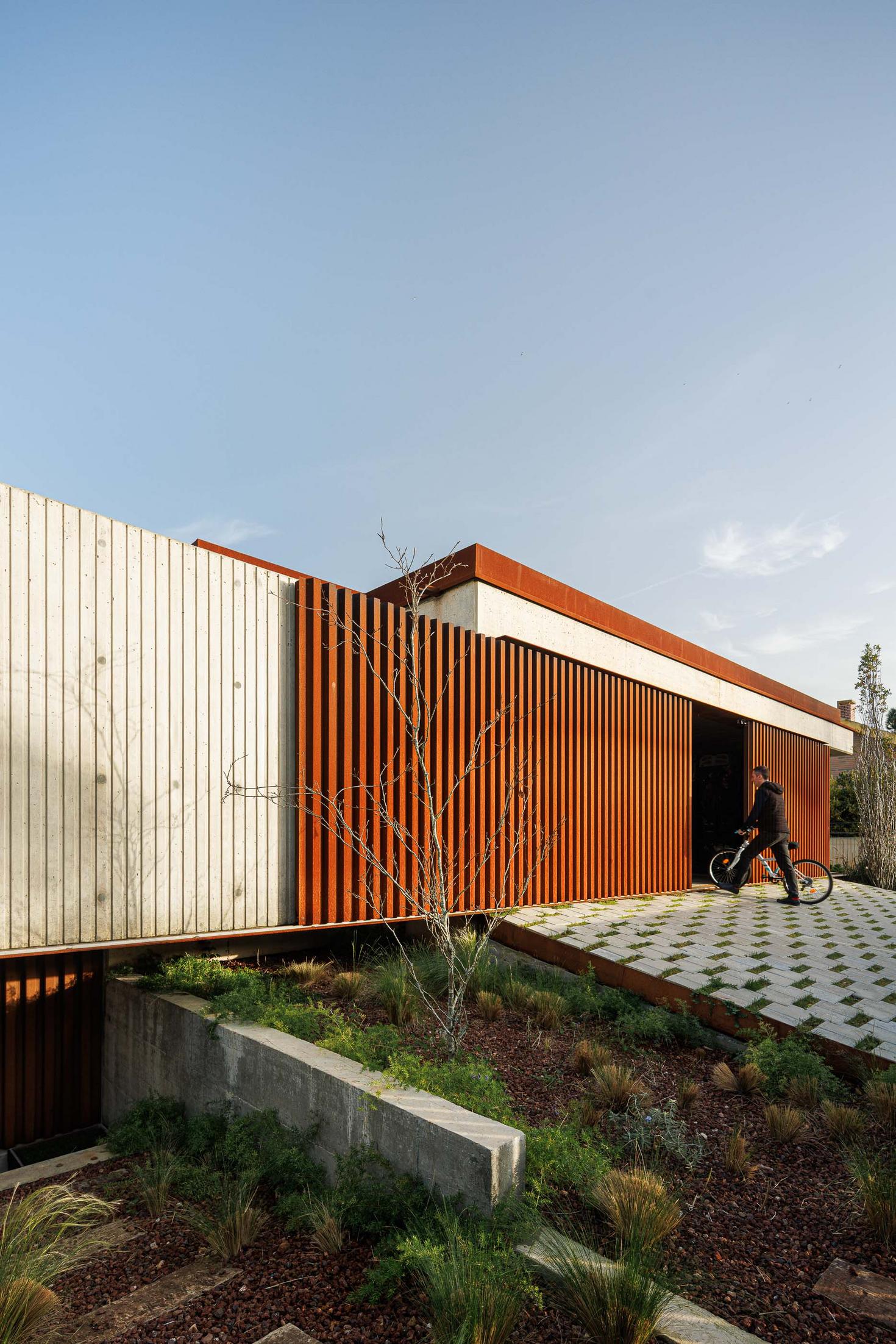 Entrada da casa com rampa de acesso, revestimento em betão e ripas de aço corten. — Mimosa House arquitetura Pedro Henrique Arquitecto em Esmoriz
