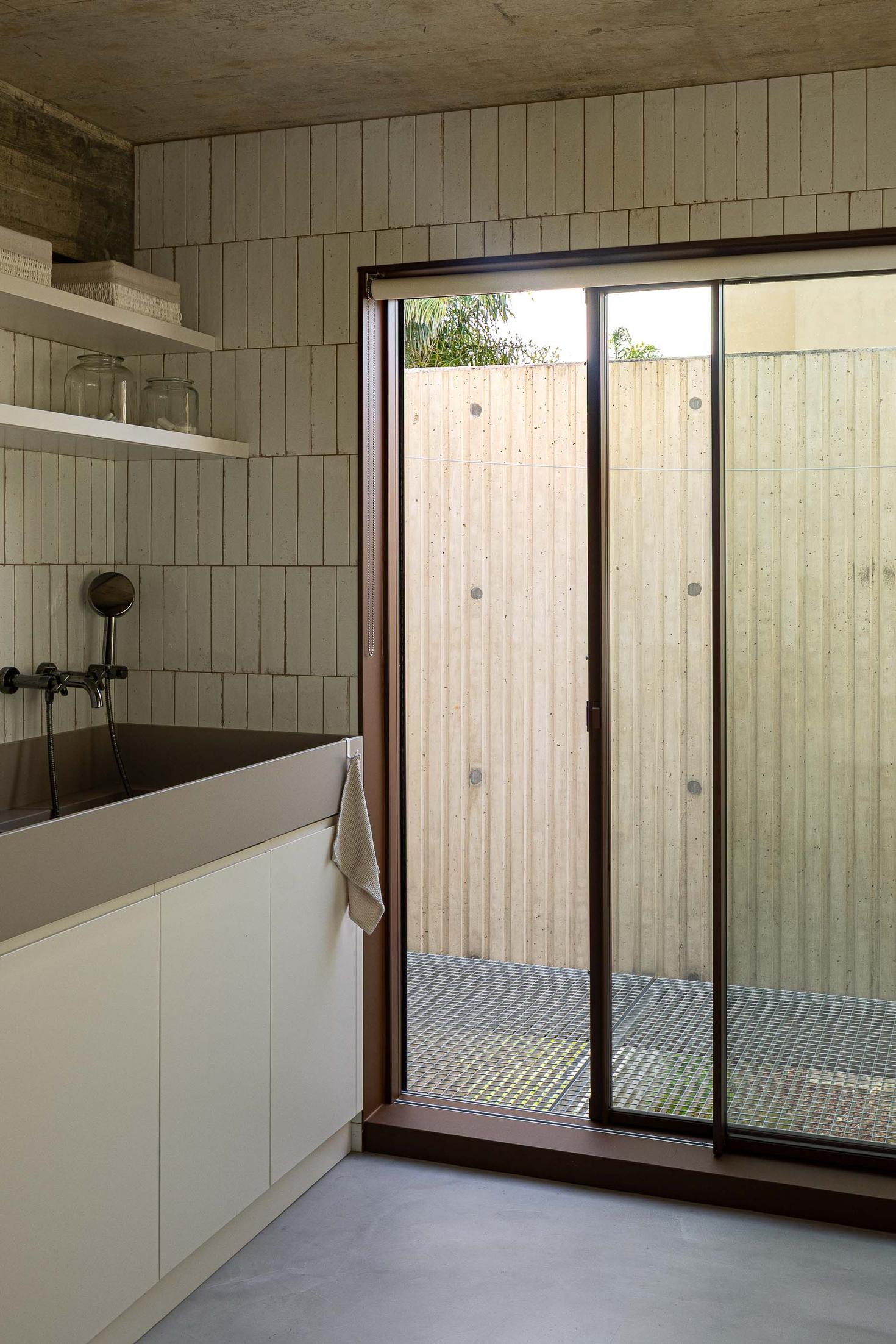 Casa de banho com lavatório em betão com torneira preta, prateleiras e janela para um pátio interior. — Mimosa House arquitetura Pedro Henrique Arquitecto em Esmoriz