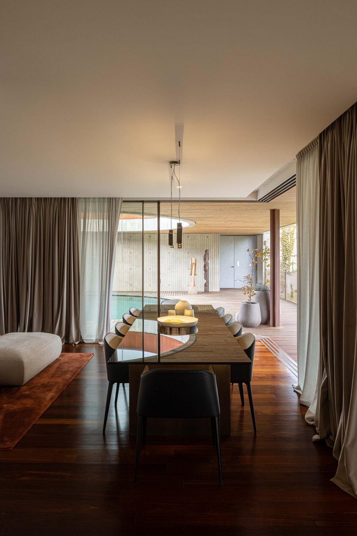 Sala de jantar com mesa comprida, cadeiras pretas e vista para a área da piscina. — Mimosa House arquitetura Pedro Henrique Arquitecto em Esmoriz