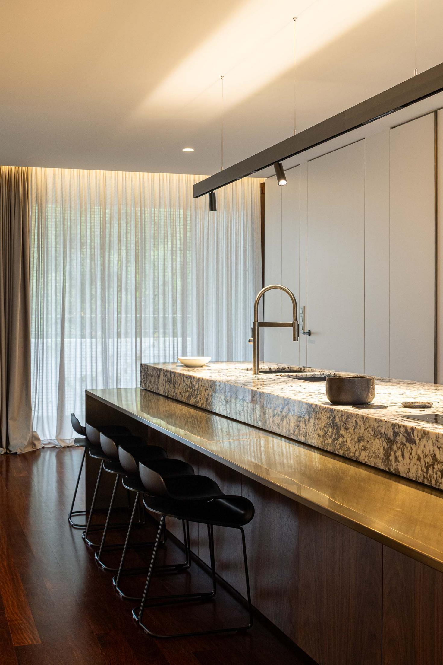 Ilha da cozinha com bancada em mármore, revestimento em latão e candeeiro suspenso. — Mimosa House arquitetura Pedro Henrique Arquitecto em Esmoriz