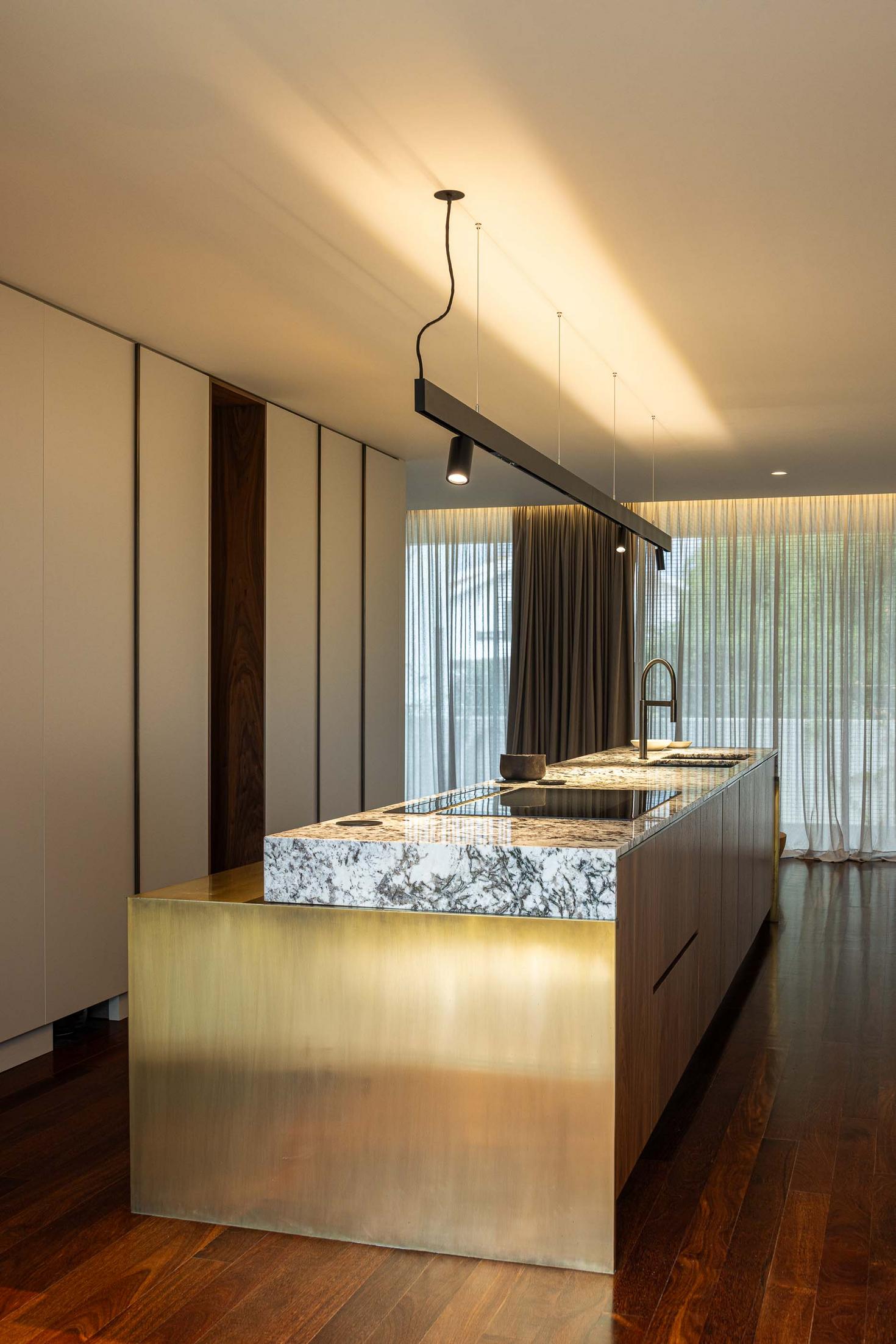 Vista geral da cozinha com ilha central, armários brancos e revestimento em latão. — Mimosa House arquitetura Pedro Henrique Arquitecto em Esmoriz