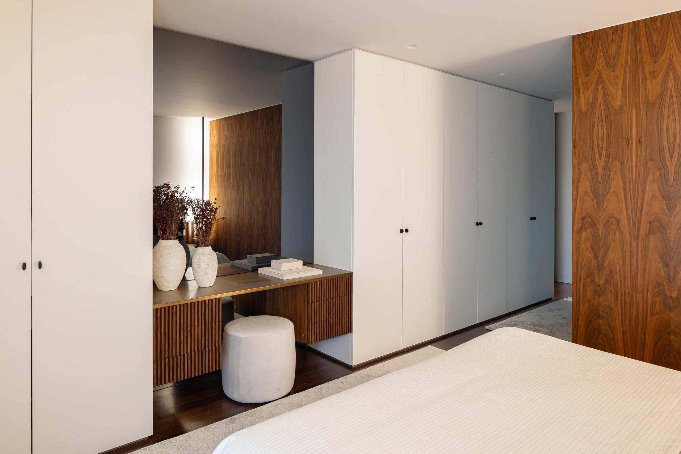 Quarto com cama de casal, armários brancos e toucador com espelho e revestimento em madeira. — Mimosa House arquitetura Pedro Henrique Arquitecto em Esmoriz