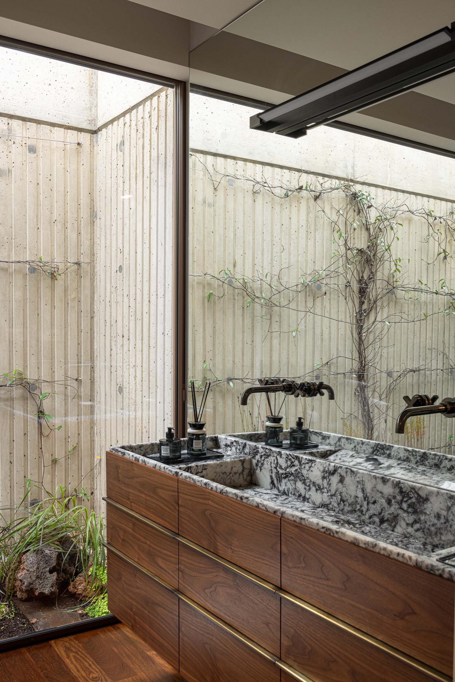 Lavatório duplo com bancada em mármore, espelho e vista para um pátio interior. — Mimosa House arquitetura Pedro Henrique Arquitecto em Esmoriz