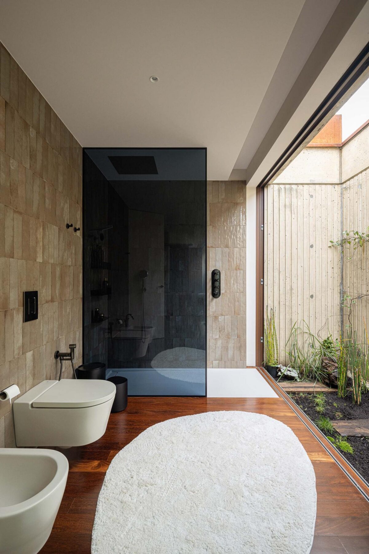 Casa de banho com duche em vidro, sanita, bidé e alcatifa branca. — Mimosa House arquitetura Pedro Henrique Arquitecto em Esmoriz