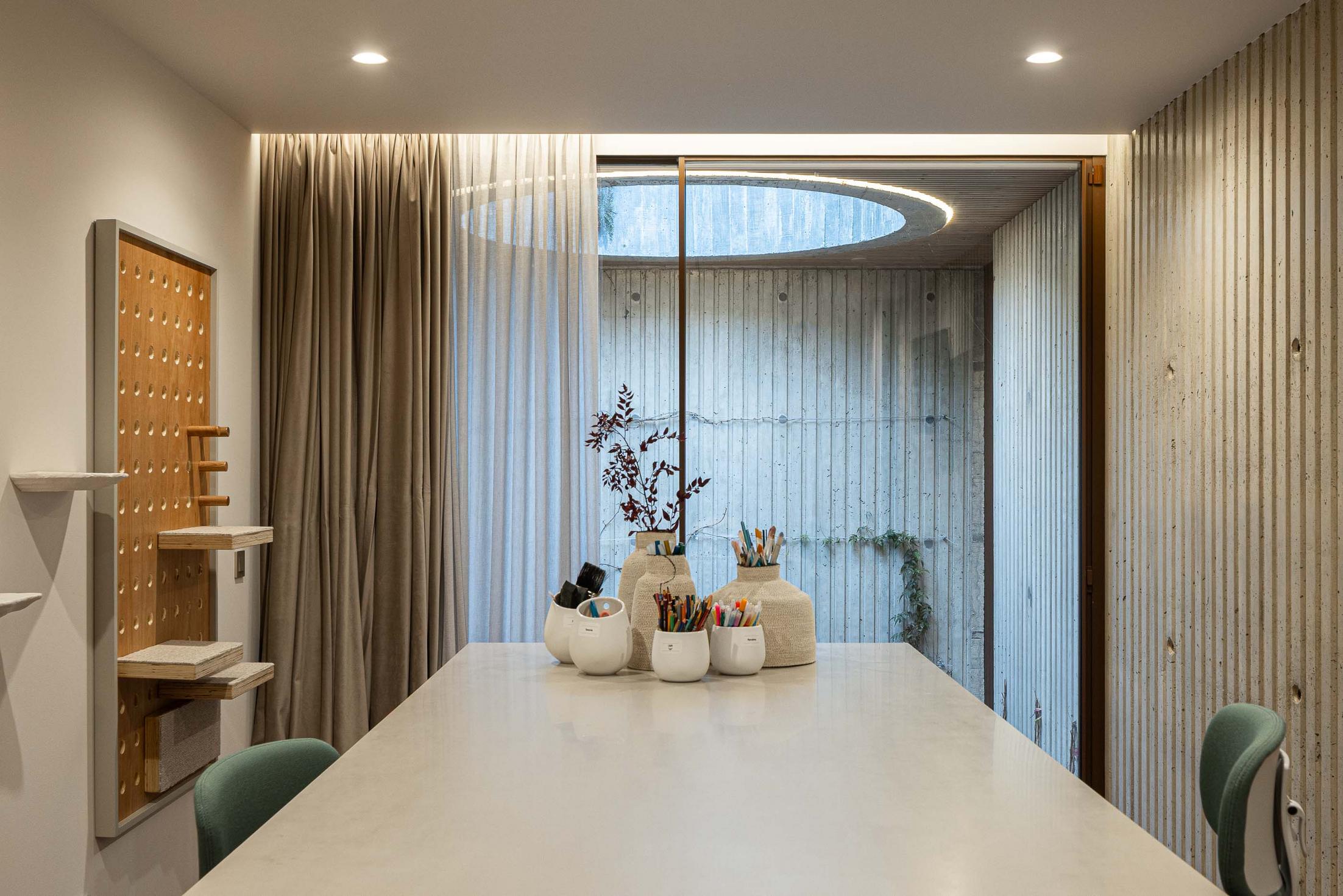 Escritório com mesa comprida, cadeiras verdes e vista para um pátio interior. — Mimosa House arquitetura Pedro Henrique Arquitecto em Esmoriz