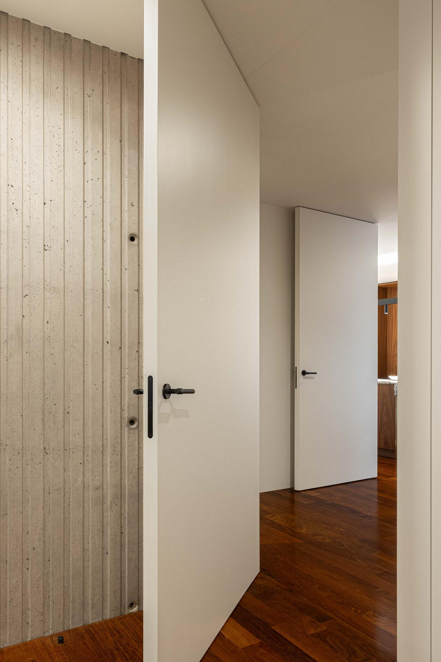 Corredor com pavimento em madeira, paredes brancas e revestimento em betão aparente. — Mimosa House arquitetura Pedro Henrique Arquitecto em Esmoriz