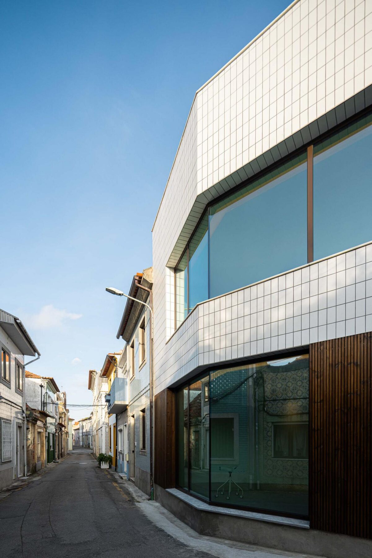 Fachada: Fachada moderna com revestimento cerâmico branco e madeira escura, grandes janelas e rua estreita. — Beira Mar II arquitetura Paulo Martins Arquitectura e Design em Aveiro