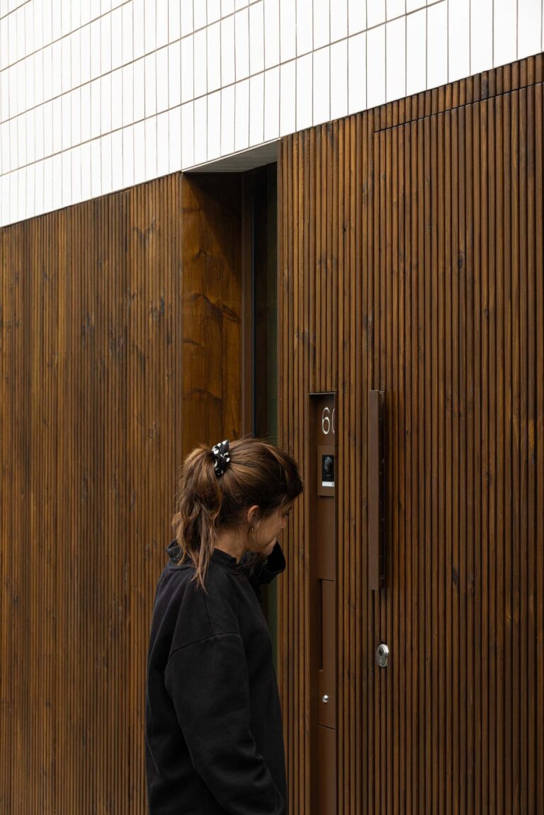 Entrada: Porta de entrada em madeira com detalhes metálicos, número 60 e mulher a tocar à campainha. — Beira Mar II arquitetura Paulo Martins Arquitectura e Design em Aveiro