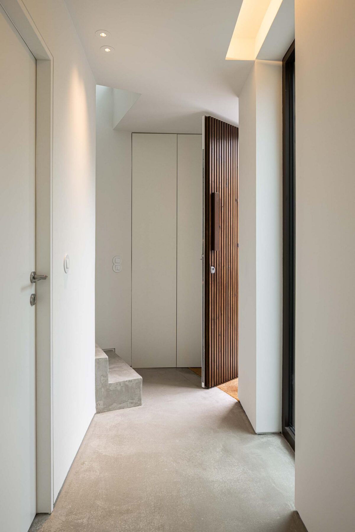 Hall de entrada: Hall branco com pavimento em cimento afagado, porta de entrada em madeira e escadas em betão. — Beira Mar II arquitetura Paulo Martins Arquitectura e Design em Aveiro