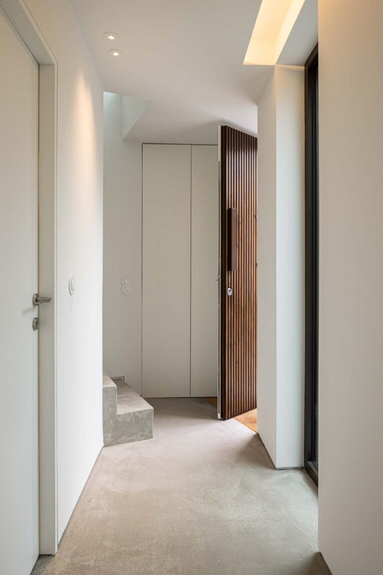 Hall de entrada: Hall branco com pavimento em cimento afagado, porta de entrada em madeira e escadas em betão. — Beira Mar II arquitetura Paulo Martins Arquitectura e Design em Aveiro