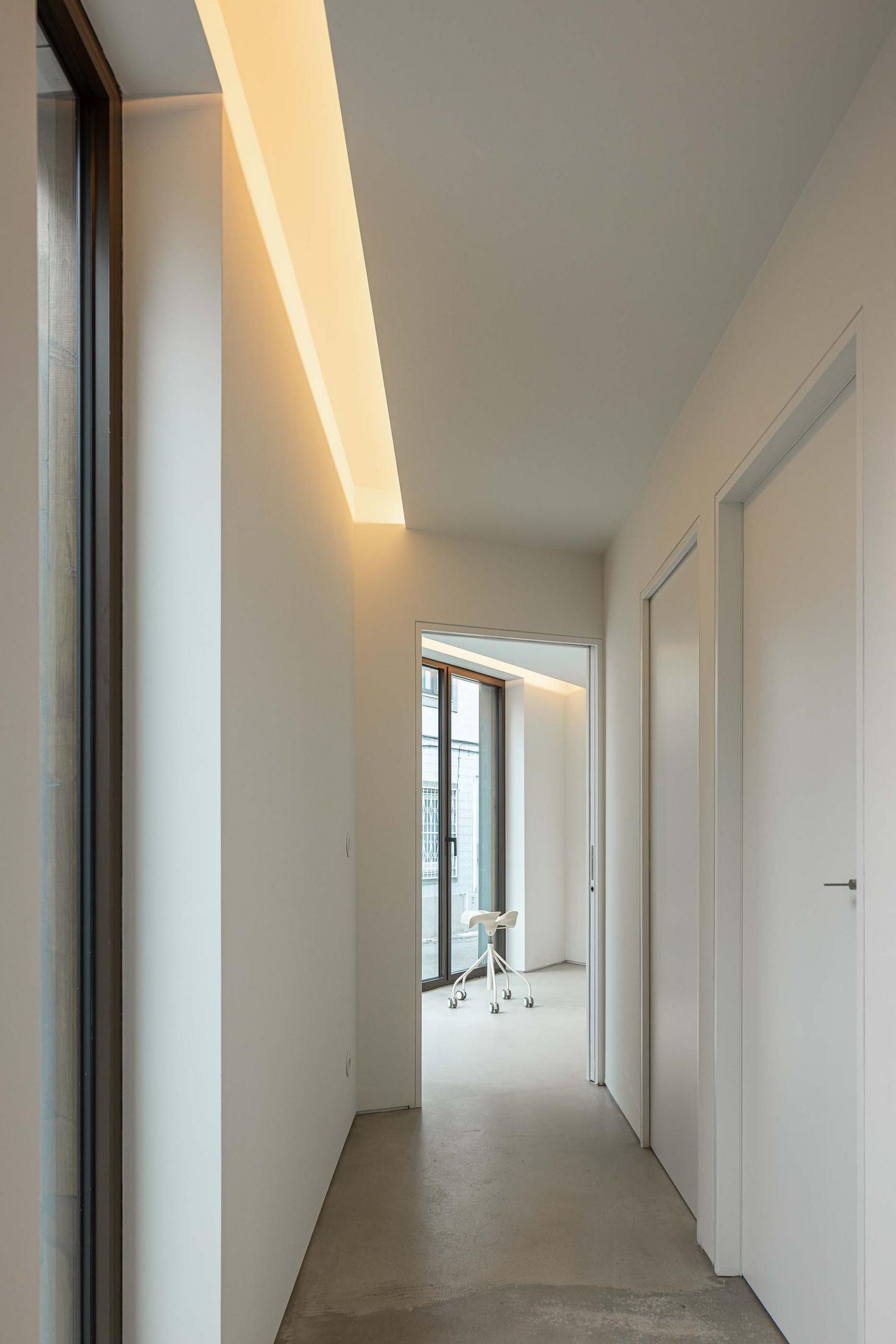 Corredor com paredes brancas e pavimento em cimento afagado. Iluminação linear embutida no teto. Portas brancas minimalistas — Beira Mar II arquitectura Paulo Martins fotografia Ivo Tavares